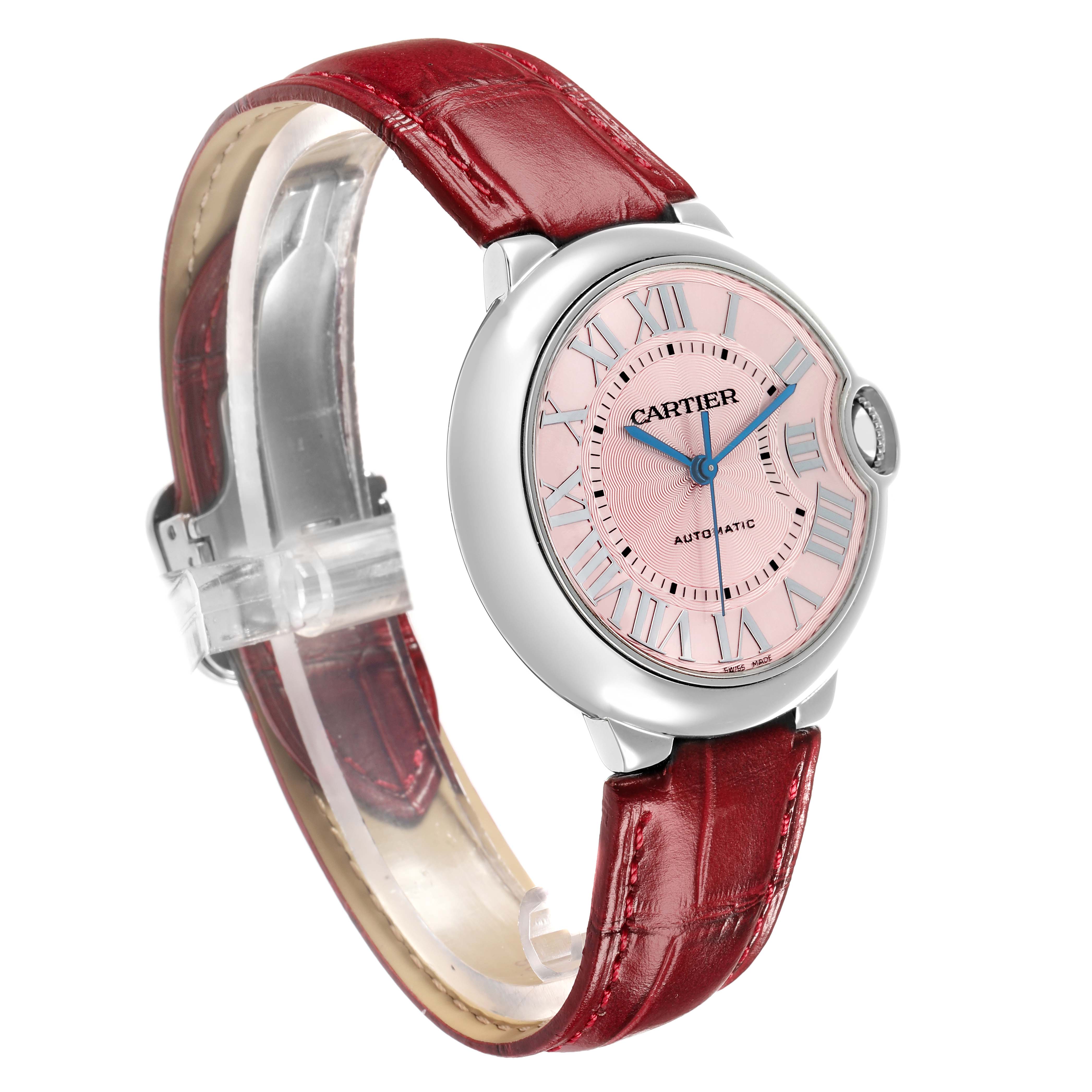 The Cartier Ballon Bleu WSBB0007 Women
s Stainless Steel Pink Dial watch is shown at an angled side view, displaying its round face, pink dial, blue hands, and red leather strap.