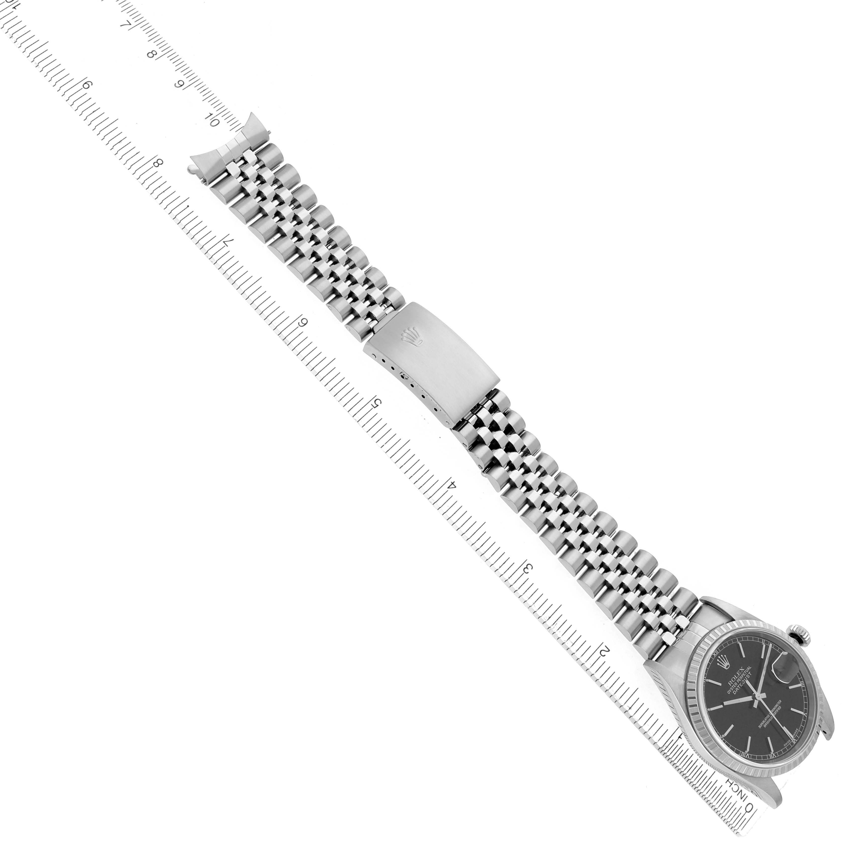 The Rolex Datejust 16220 Men
s Stainless Steel Black Dial watch is shown at an angle, highlighting the face, bracelet, and clasp, displayed alongside a ruler.