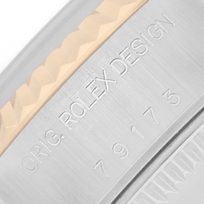 The image shows a close-up of the Rolex Datejust 79173 Women
s Steel and Gold (two tone) Silver Dial watch
s bezel and engraved text on the side of the case.