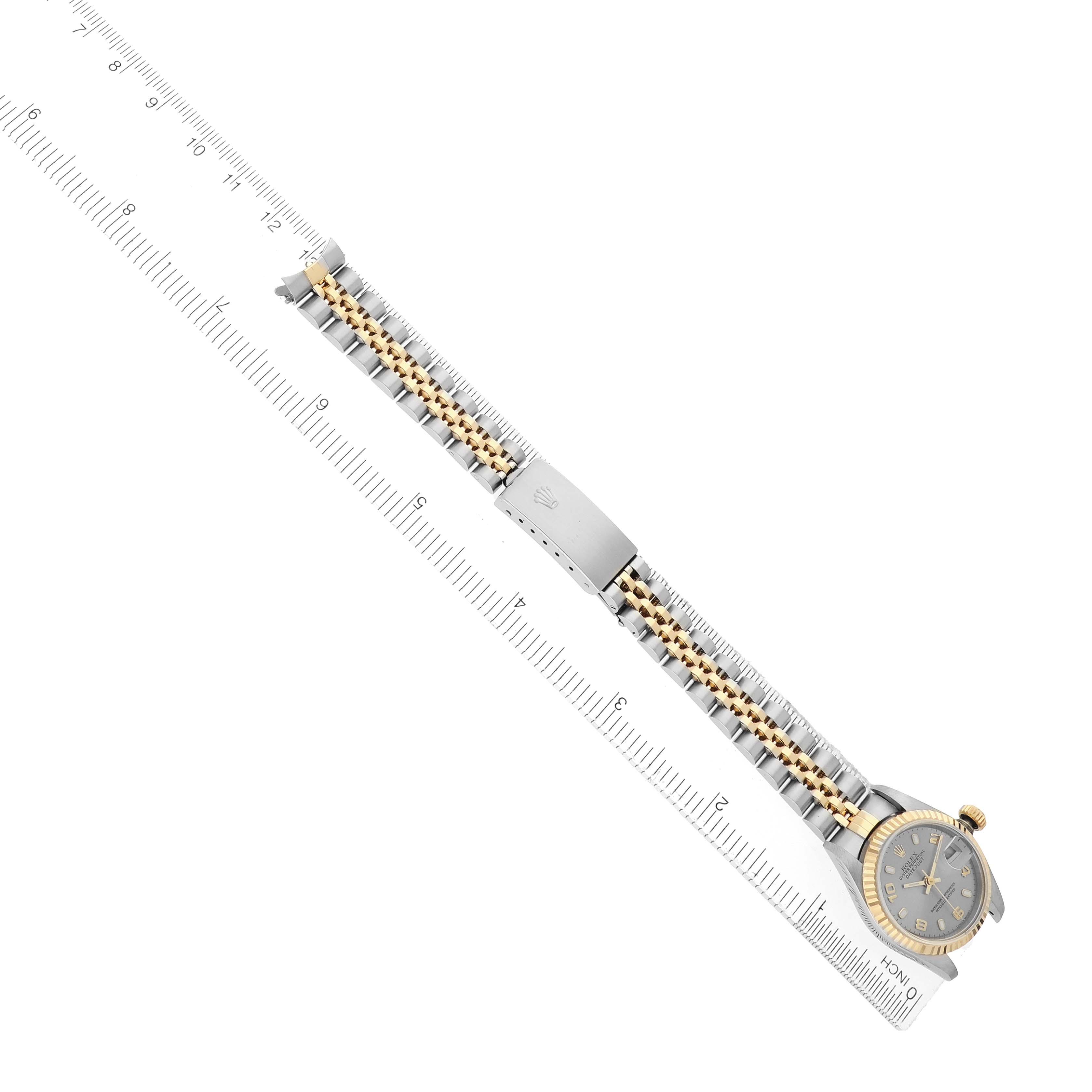 The Rolex Datejust 79173 Women
s Steel and Gold (two tone) Silver Dial watch is shown from a top-down perspective, displaying its bracelet and face alongside a ruler.