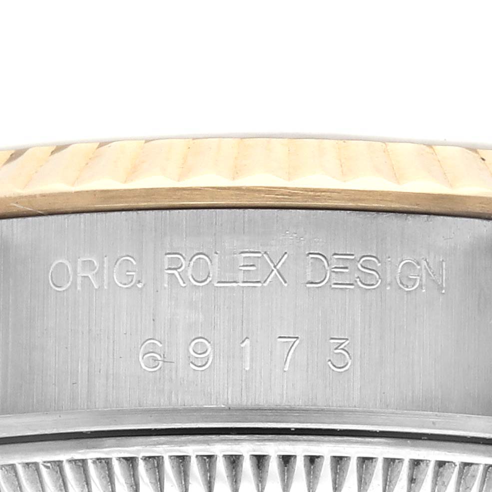 The image shows a macro angle of the Rolex Datejust 69173 Women
s Steel and Gold (two tone) Champagne Dial model
s fluted bezel and engraved design number.