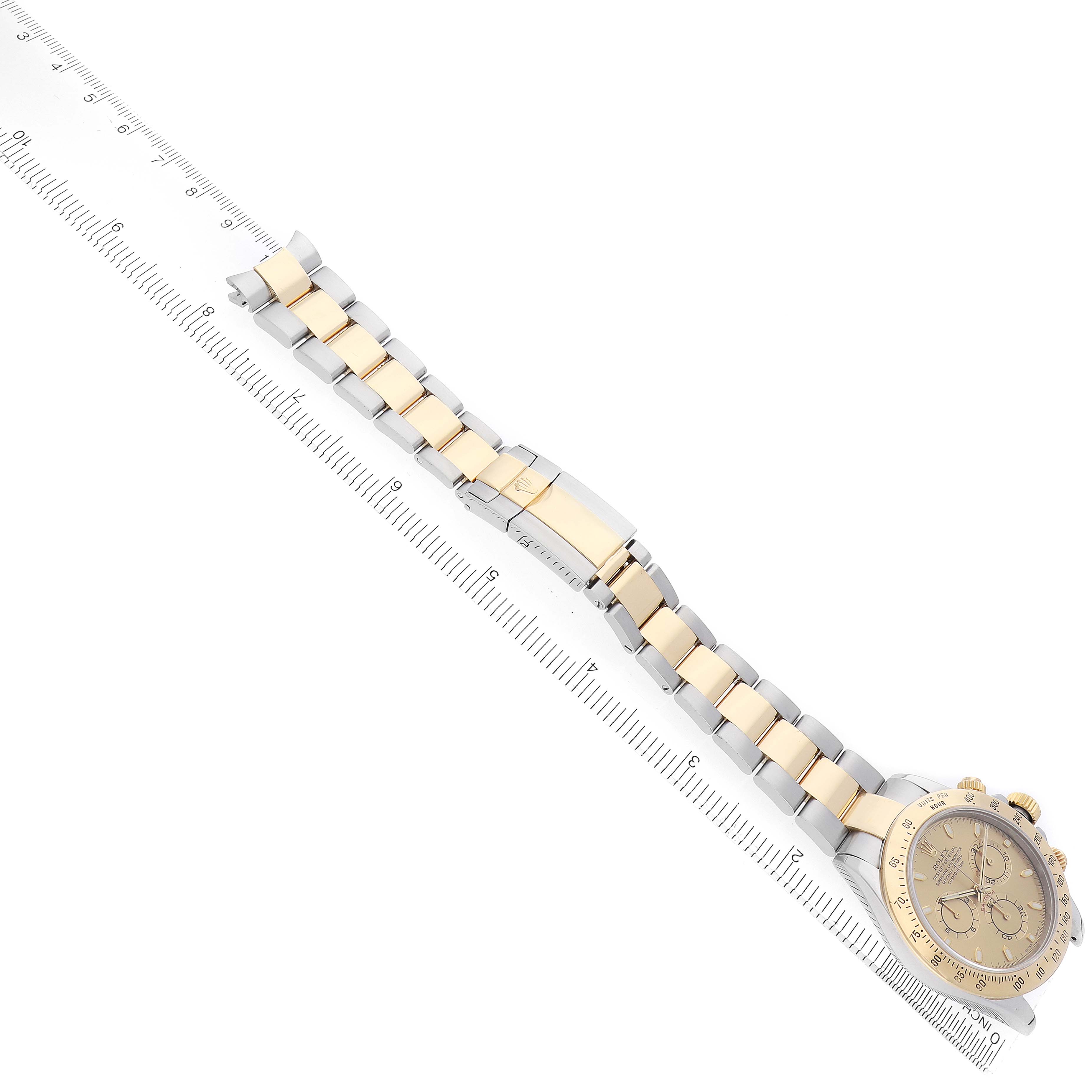 The Rolex Daytona 116523 Men
s Steel and Gold (two tone) Champagne Dial watch is shown diagonally, highlighting its gold and stainless steel bracelet alongside a ruler.