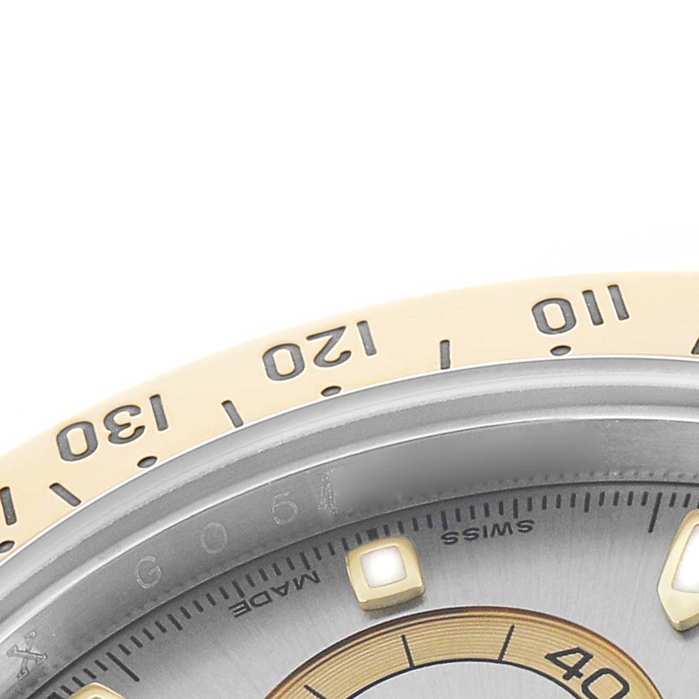 The image shows a close-up of the bezel and a portion of the dial of a Rolex Daytona 116523 Men
s Steel and Gold (two tone) Silver Dial watch.