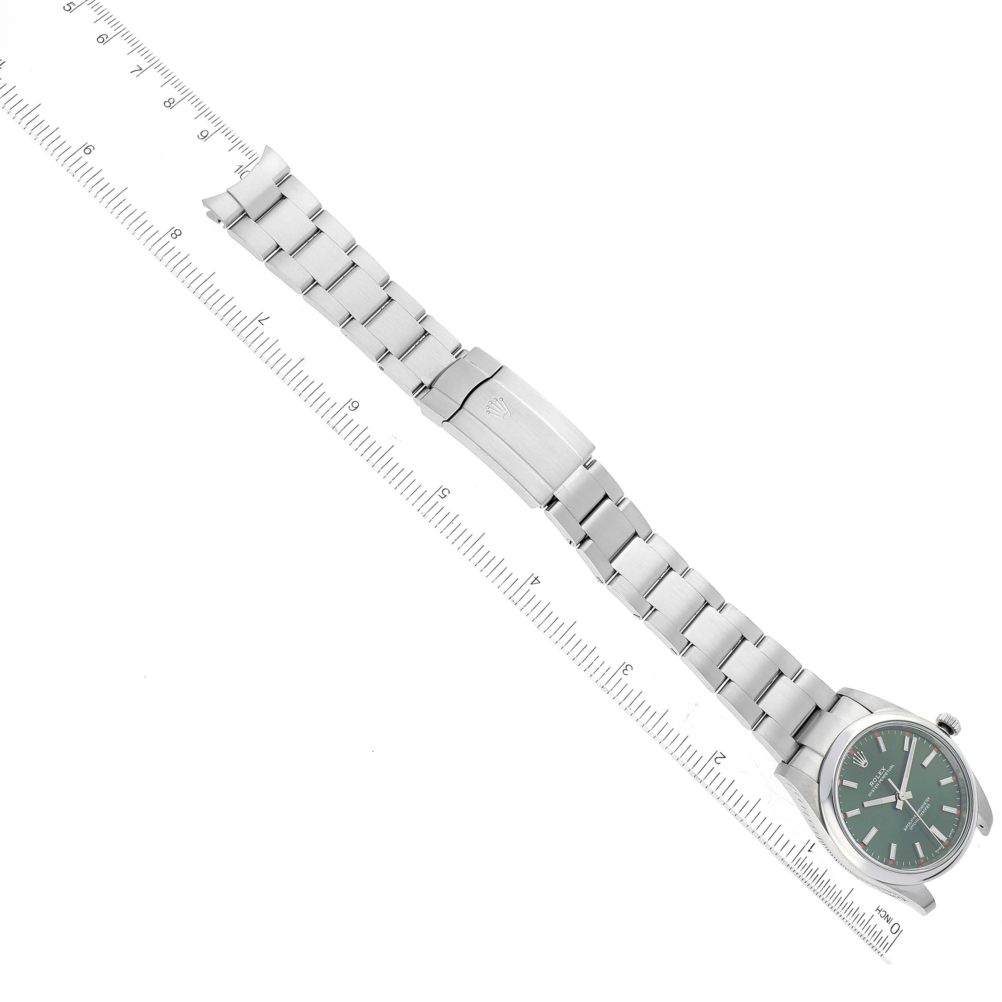 The image shows a top view of a Rolex Oyster Perpetual 114200 Men
s Stainless Steel Green Dial 114200 Men
s Stainless Steel Green Dial watch, highlighting its green dial, case, and bracelet with a ruler for scale.