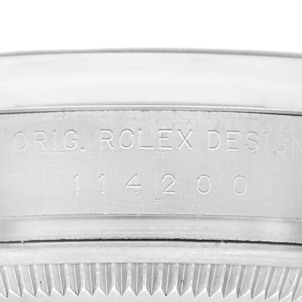 This image shows a close-up of the engraved case back and bezel edge of a Rolex Oyster Perpetual 114200 Men
s Stainless Steel Green Dial 114200 Men
s Stainless Steel Green Dial watch.