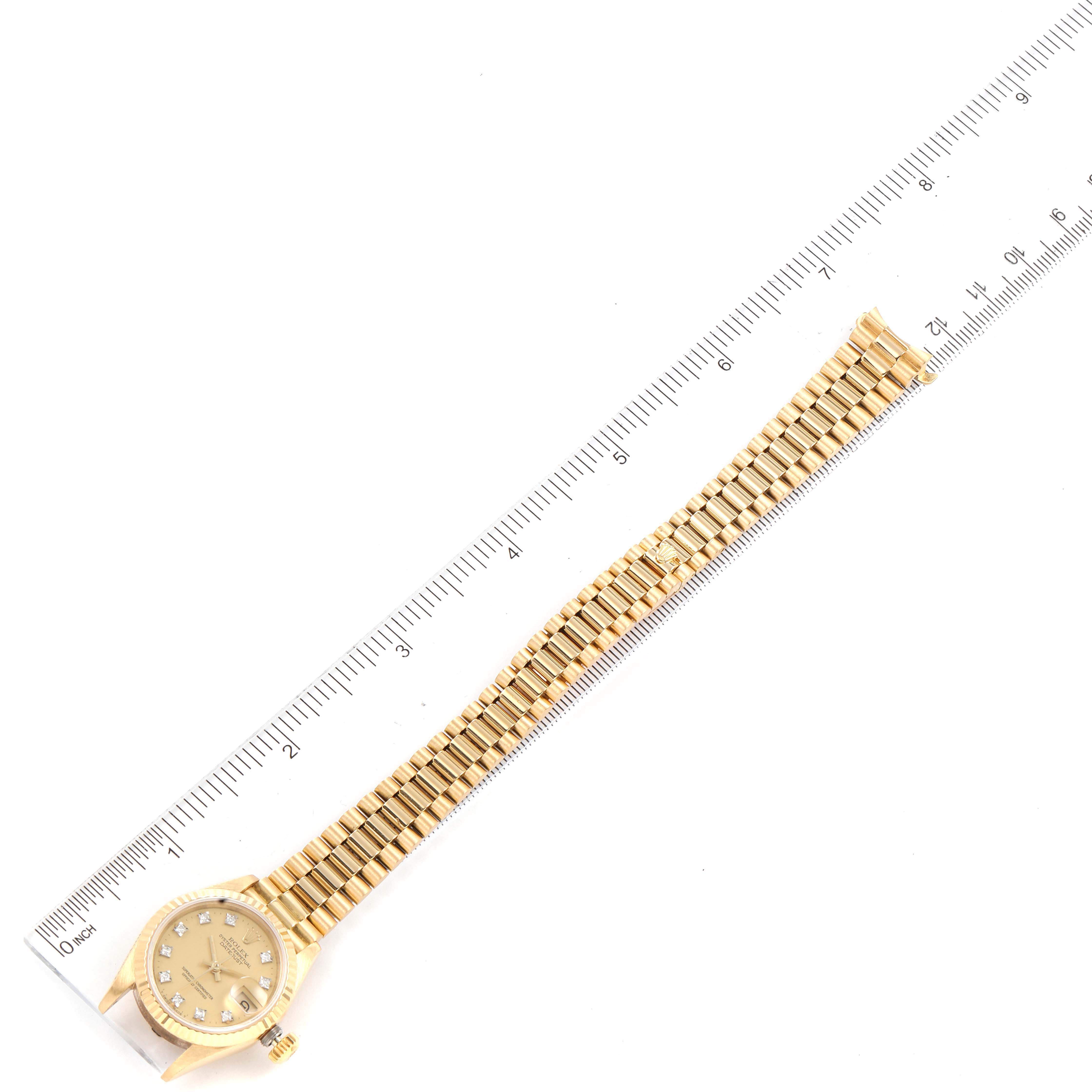 The Rolex President 69178 Women's Yellow Gold Champagne Dial 69178 Women's Yellow Gold Champagne Dial model watch is shown at an overhead angle, displaying its face, bracelet, and partial bezel against a ruler for scale.