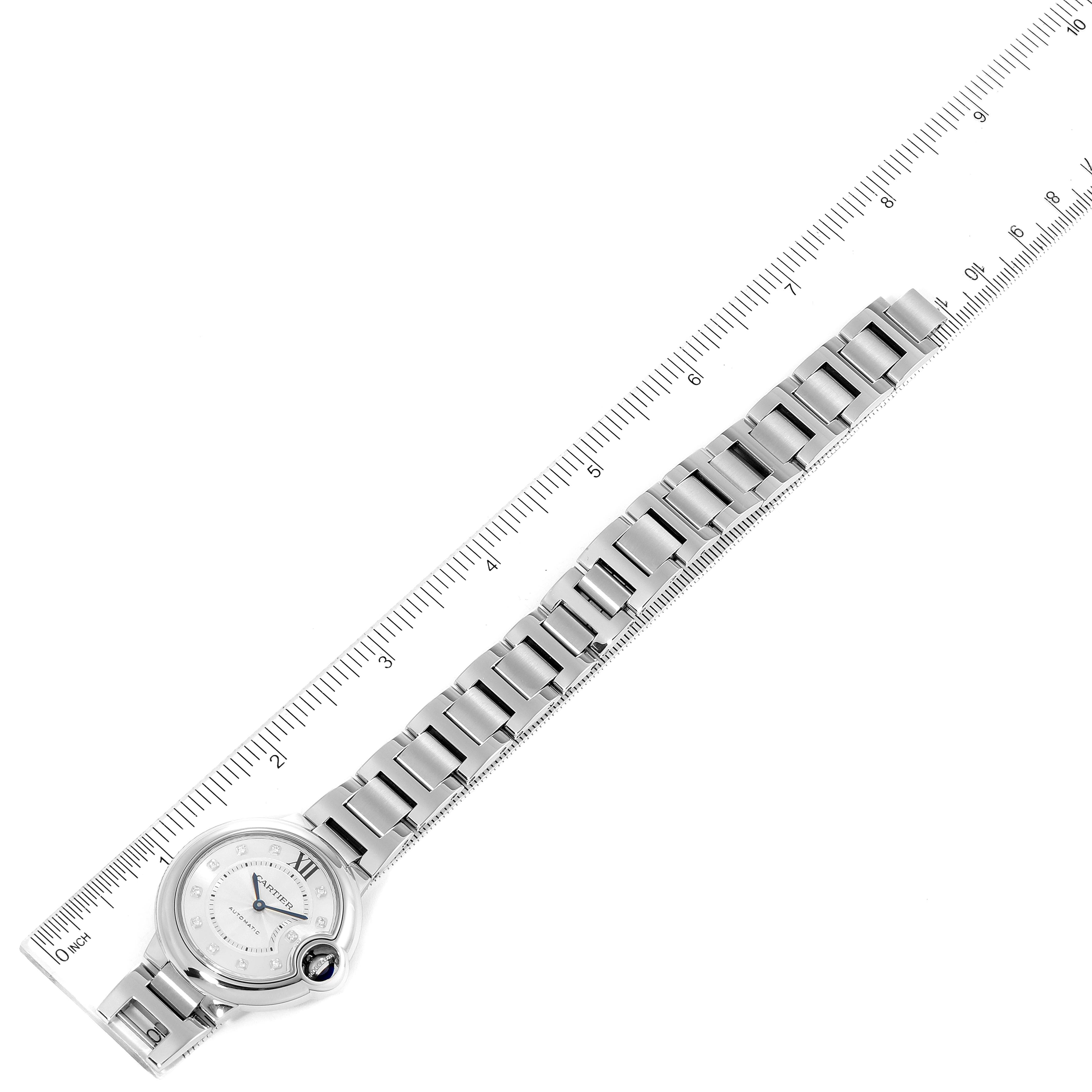 The image shows an overhead view of a Cartier Ballon Bleu WE902074 Women
s Stainless Steel Silver Dial WE902074 Women
s Stainless Steel Silver Dial watch with its metal bracelet laid flat next to a ruler for scale.