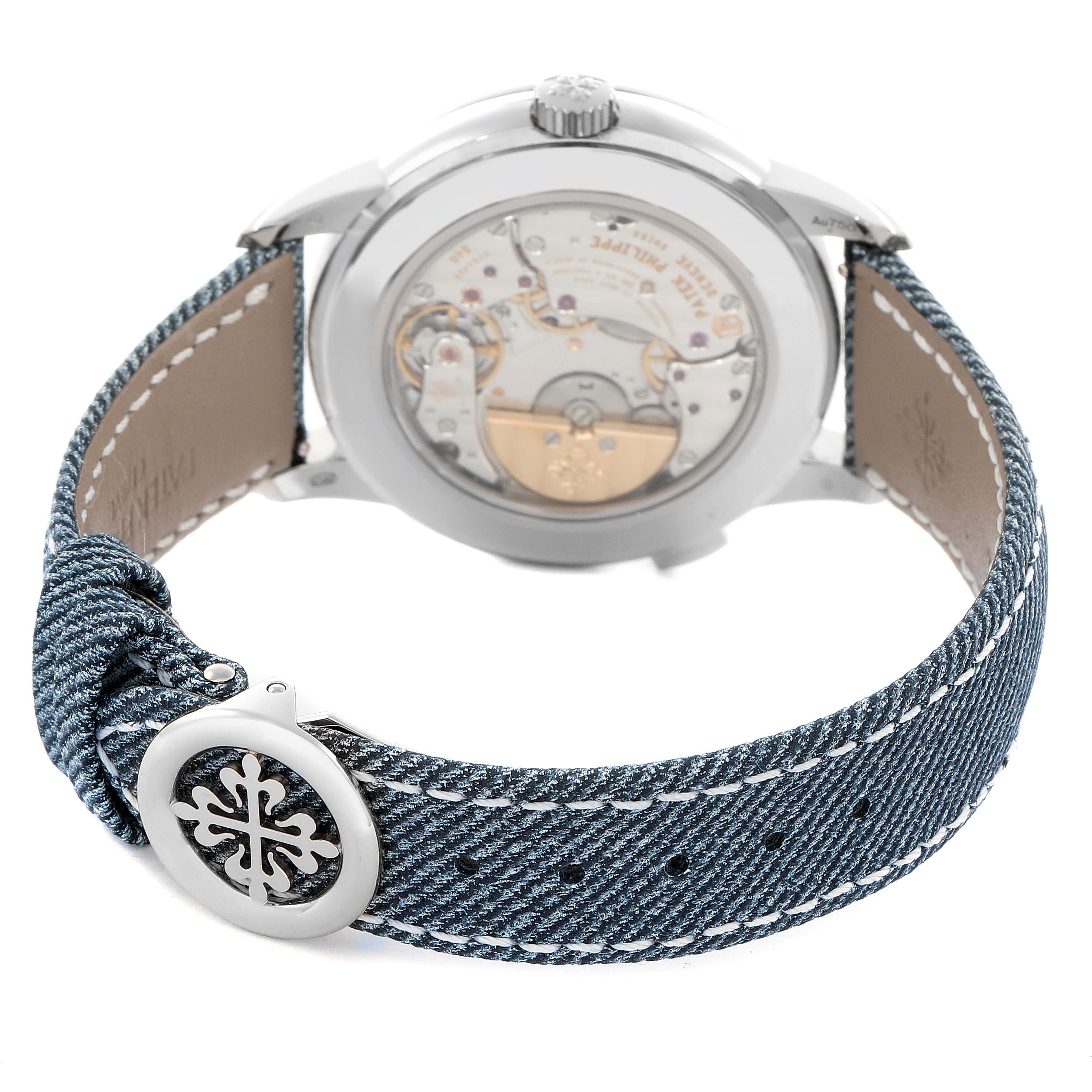 The image shows the back of the Patek Philippe Complications 5330G Men
s White Gold Blue Dial watch, highlighting the intricate movement and denim strap with logo detail.
