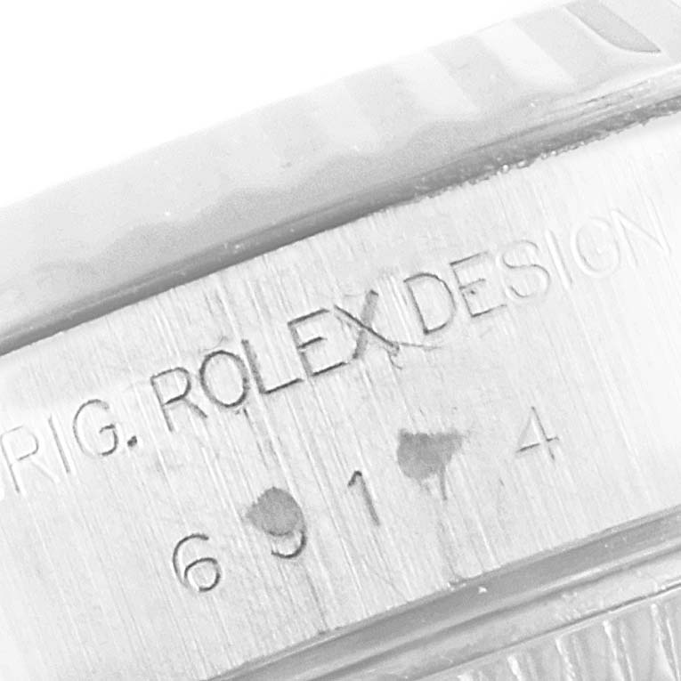 The image shows a close-up of the engraved serial number and "ROLEX DESIGN" on the case of a Rolex Datejust 69174 Women
s Stainless Steel Silver Dial 69174 Women
s Stainless Steel Silver Dial watch.