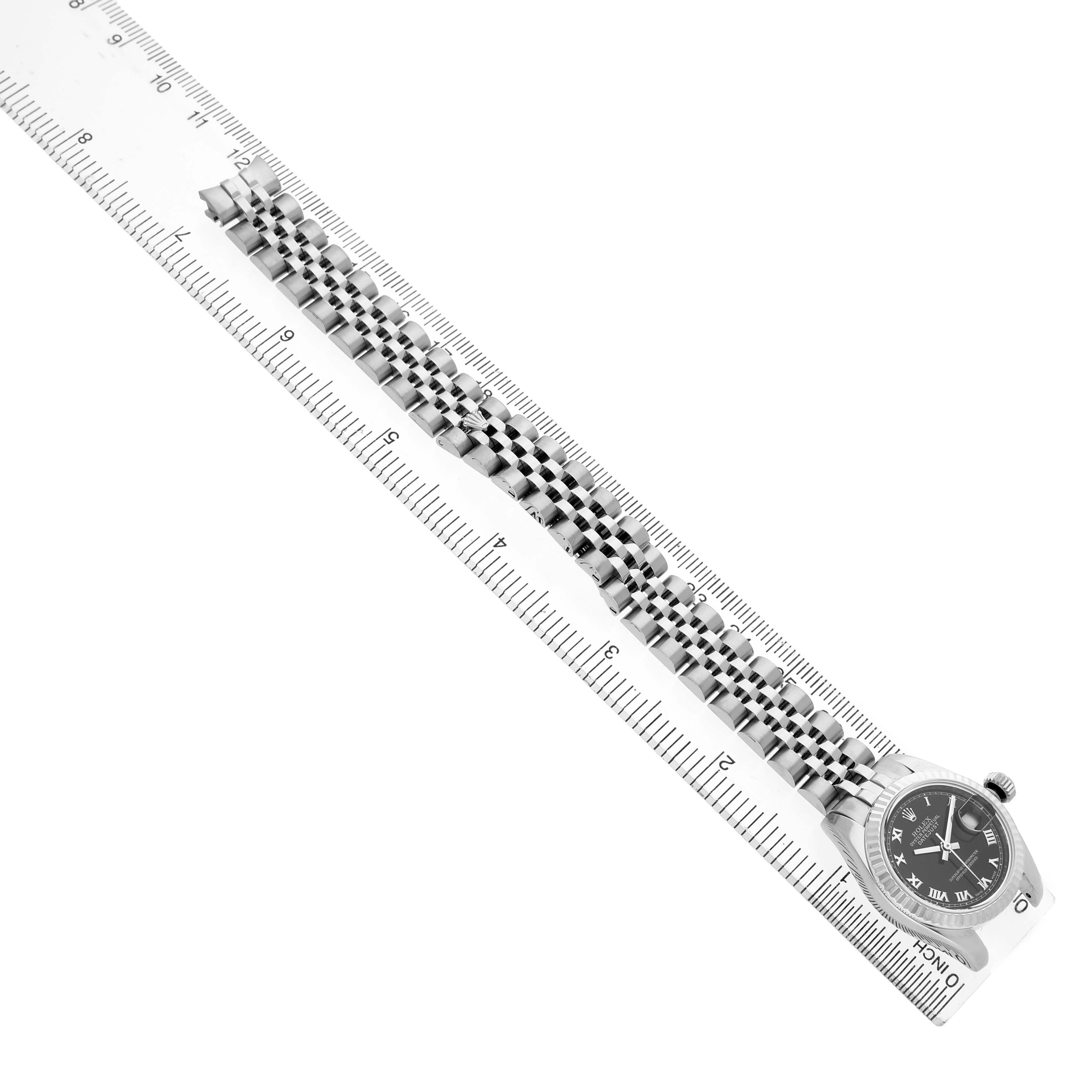 The Rolex Datejust 179174 Women's Stainless Steel Black Dial watch is shown from a top view, displaying its bracelet and dial next to a ruler for scale.