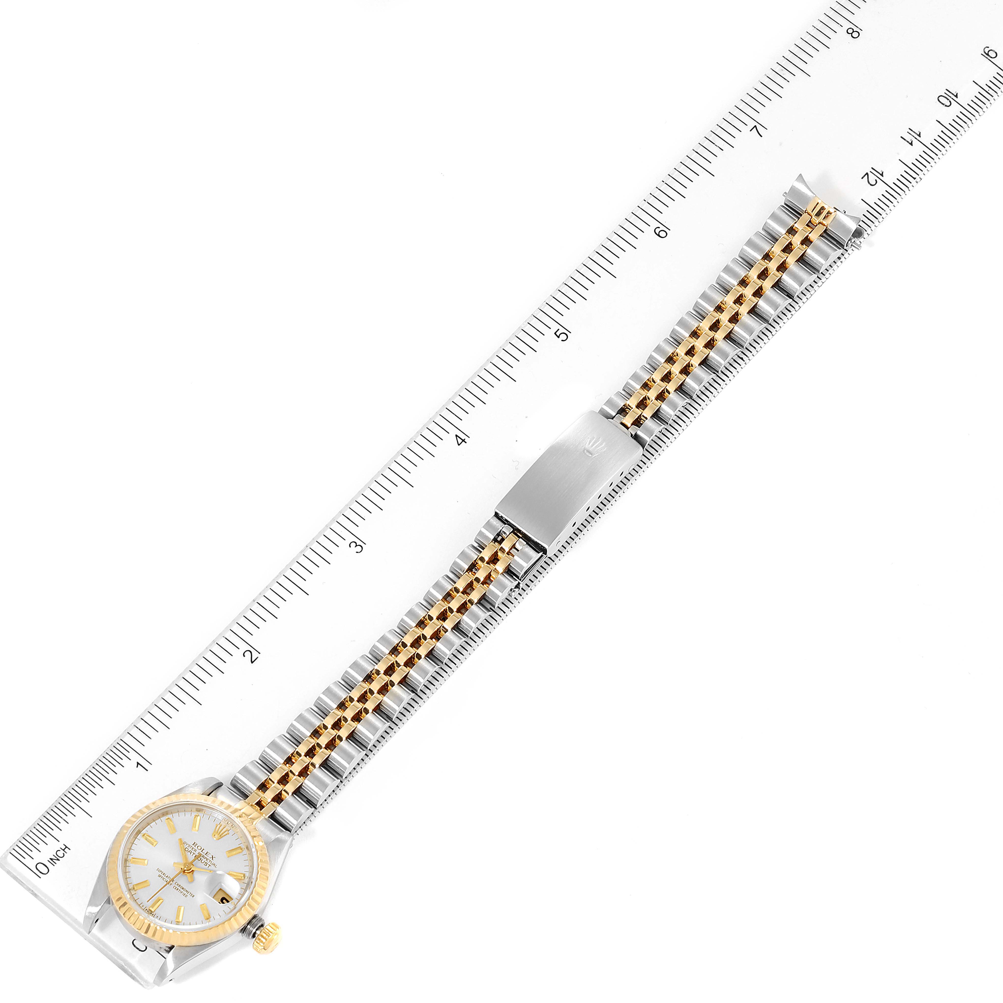 This image shows a top-down view of a Rolex Datejust 69173 Women
s Steel and Gold (two tone) Silver Dial 69173 Women
s Steel and Gold (two tone) Silver Dial watch alongside a ruler displaying its dial, bezel, and two-tone bracelet.