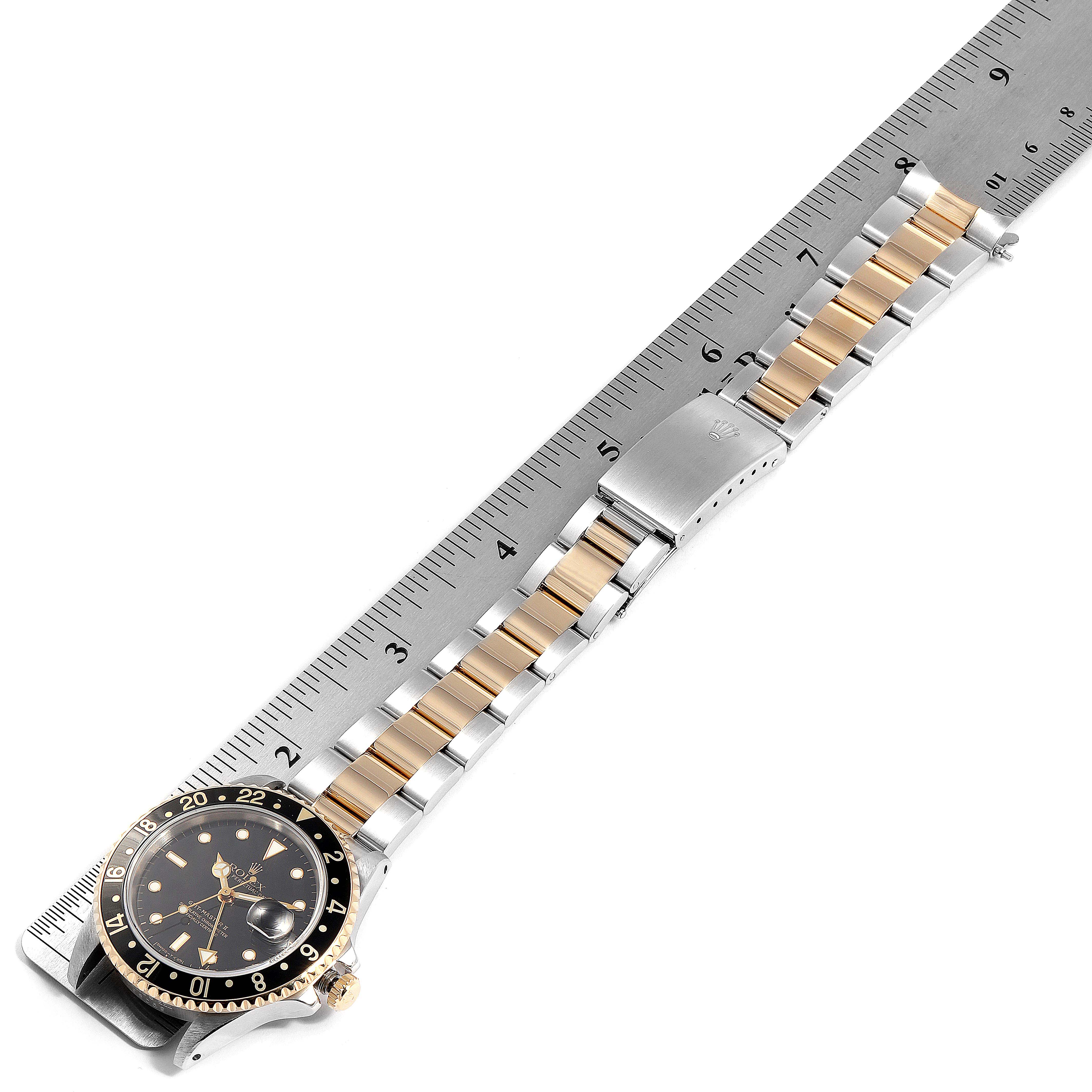 The image shows a top view of a Rolex GMT-Master 16713 Men's Steel and Gold (two tone) Black Dial 16713 Men's Steel and Gold (two tone) Black Dial watch, including the bezel, dial, and two-tone bracelet, placed alongside a ruler.