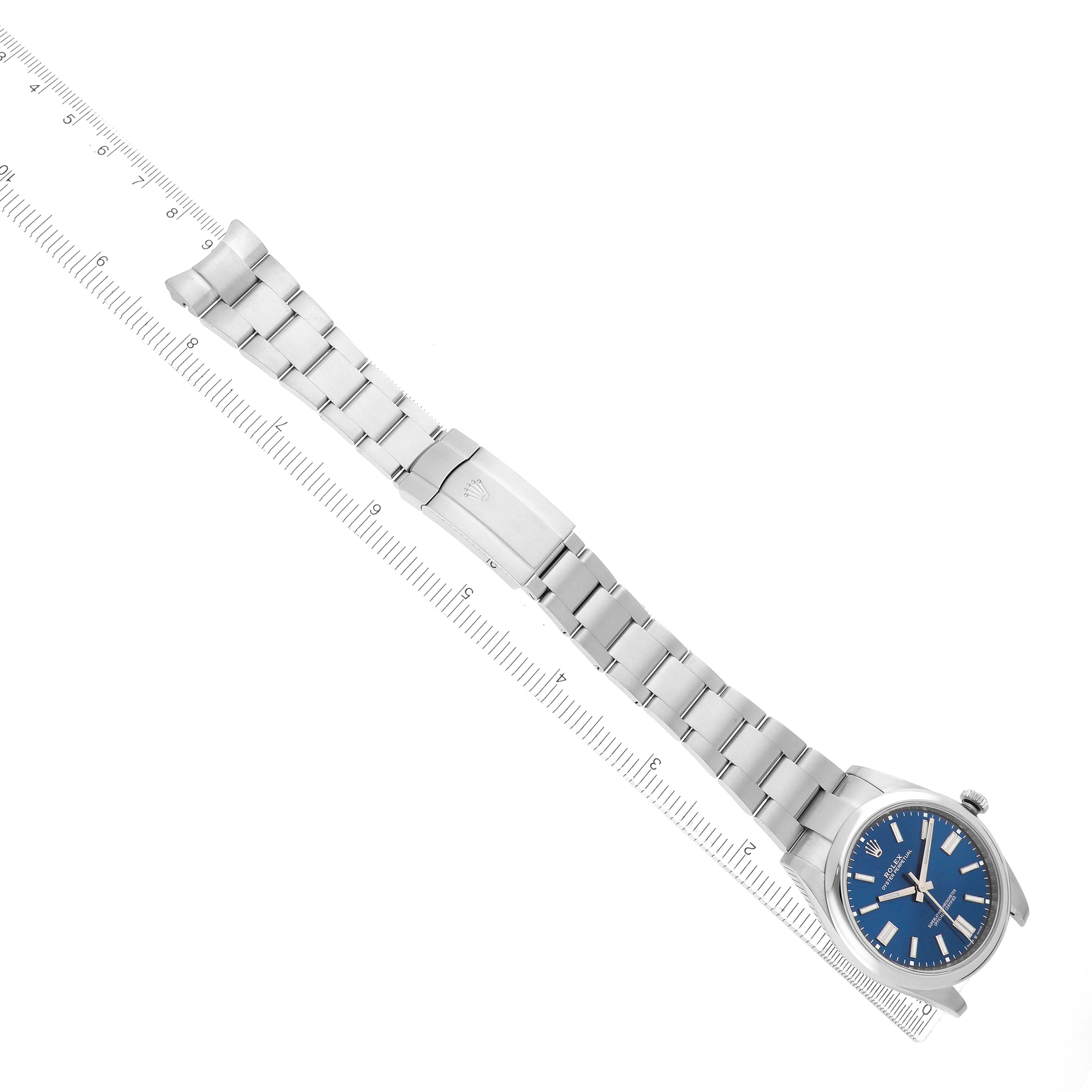 The Rolex Oyster Perpetual 124300 Men
s Stainless Steel Blue Dial is displayed diagonally with a full view of the bracelet and clasp, next to a ruler for scale.