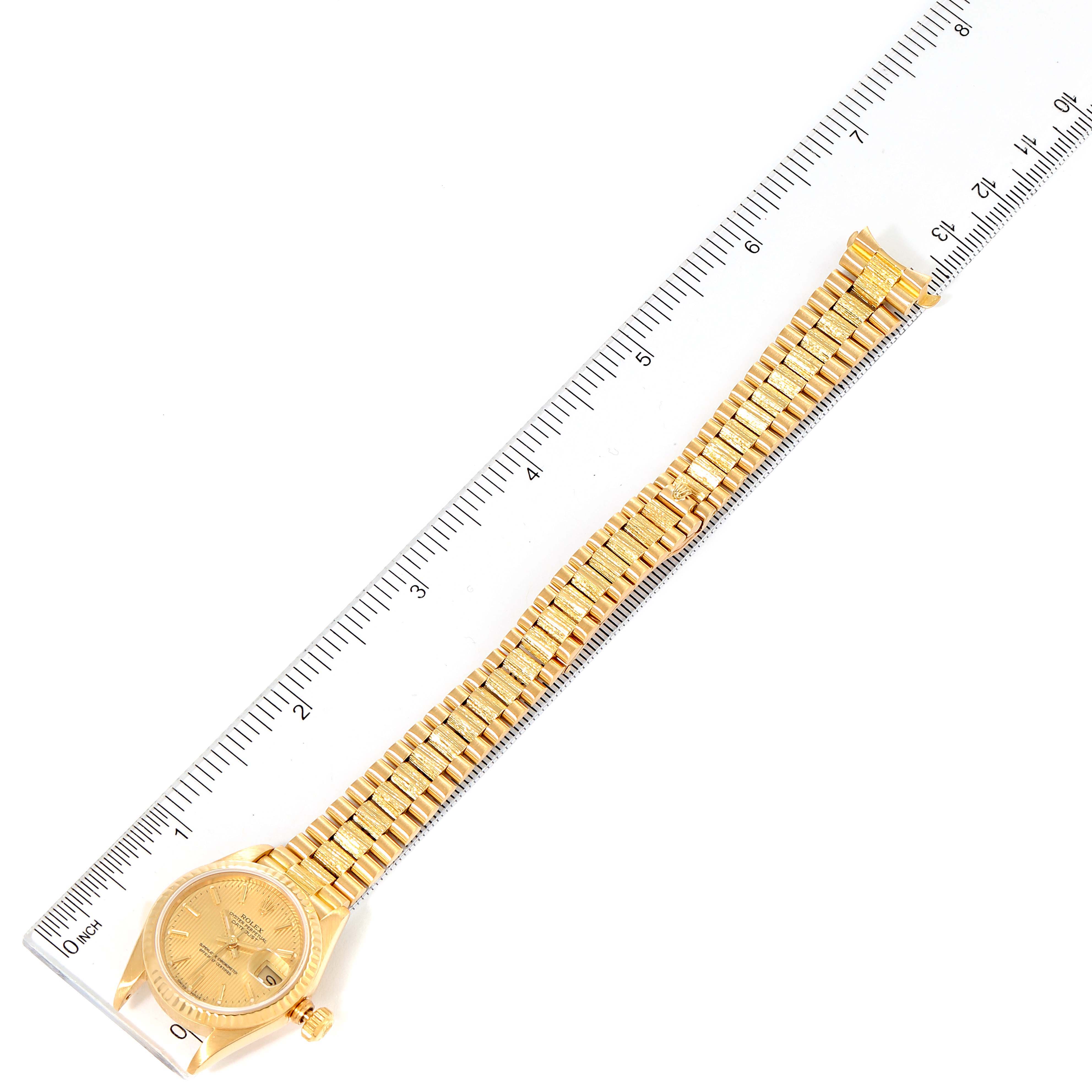 The Rolex President 69178 Women's Yellow Gold Champagne Dial 69178 Women's Yellow Gold Champagne Dial model watch is shown from an overhead angle, displaying the face, bezel, case, and bracelet next to a ruler.