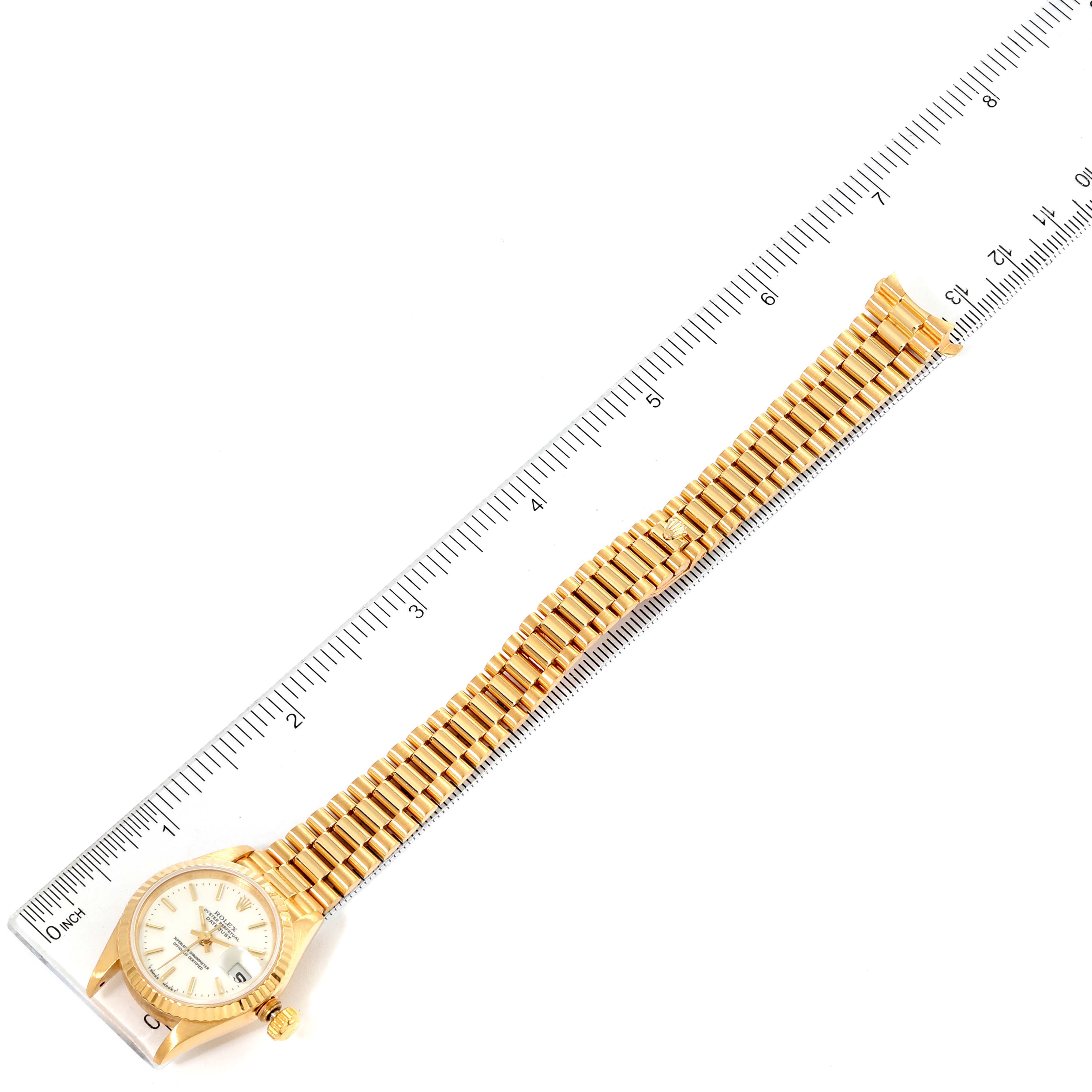 The image shows a top-down view of a Rolex President 69178 Women's Yellow Gold White Dial 69178 Women's Yellow Gold White Dial model watch alongside a ruler for size reference, highlighting the wristband and face.