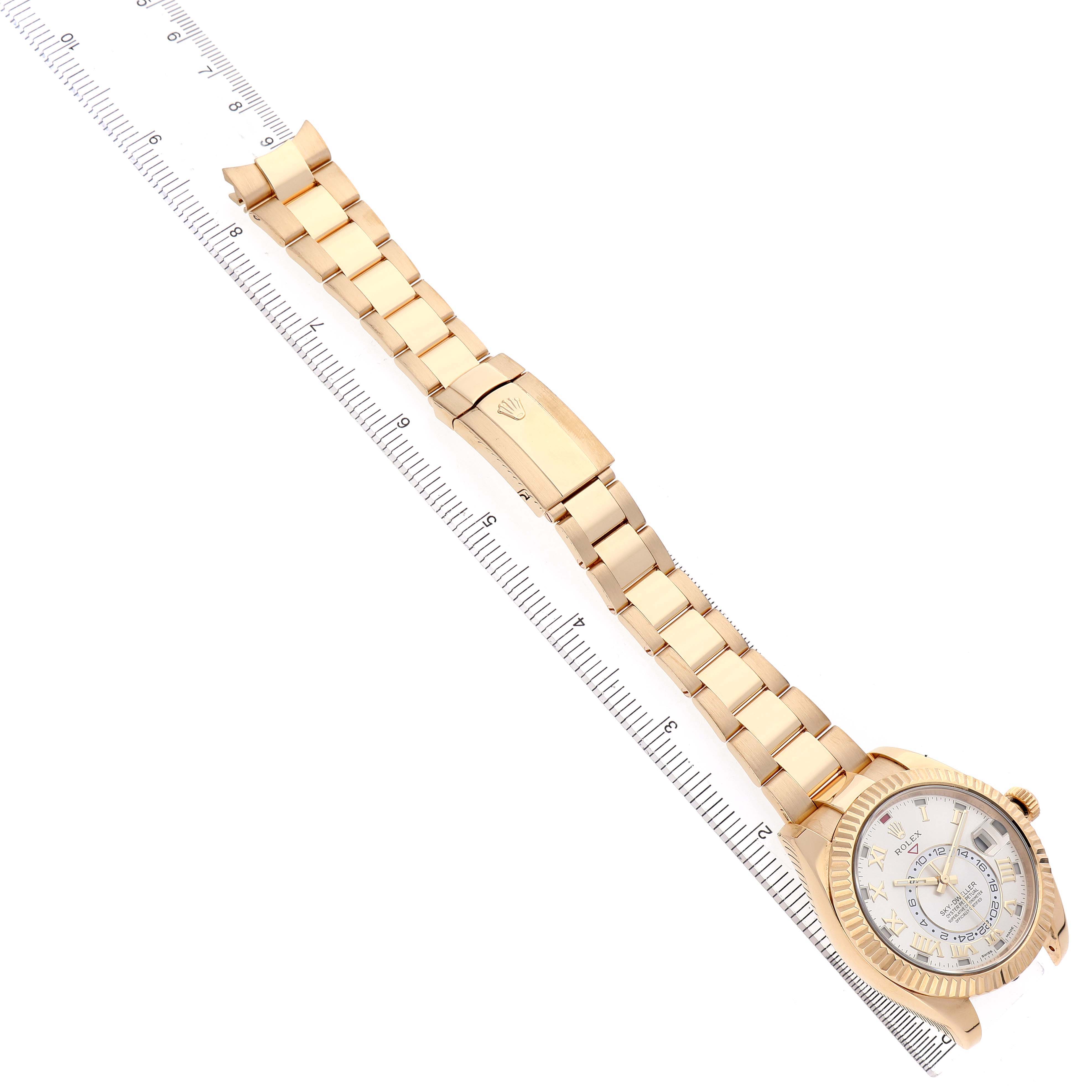 The Rolex Sky-Dweller 326938 Men's Yellow Gold Silver Dial watch is shown at an angle displaying the full watch and bracelet extended next to a ruler.