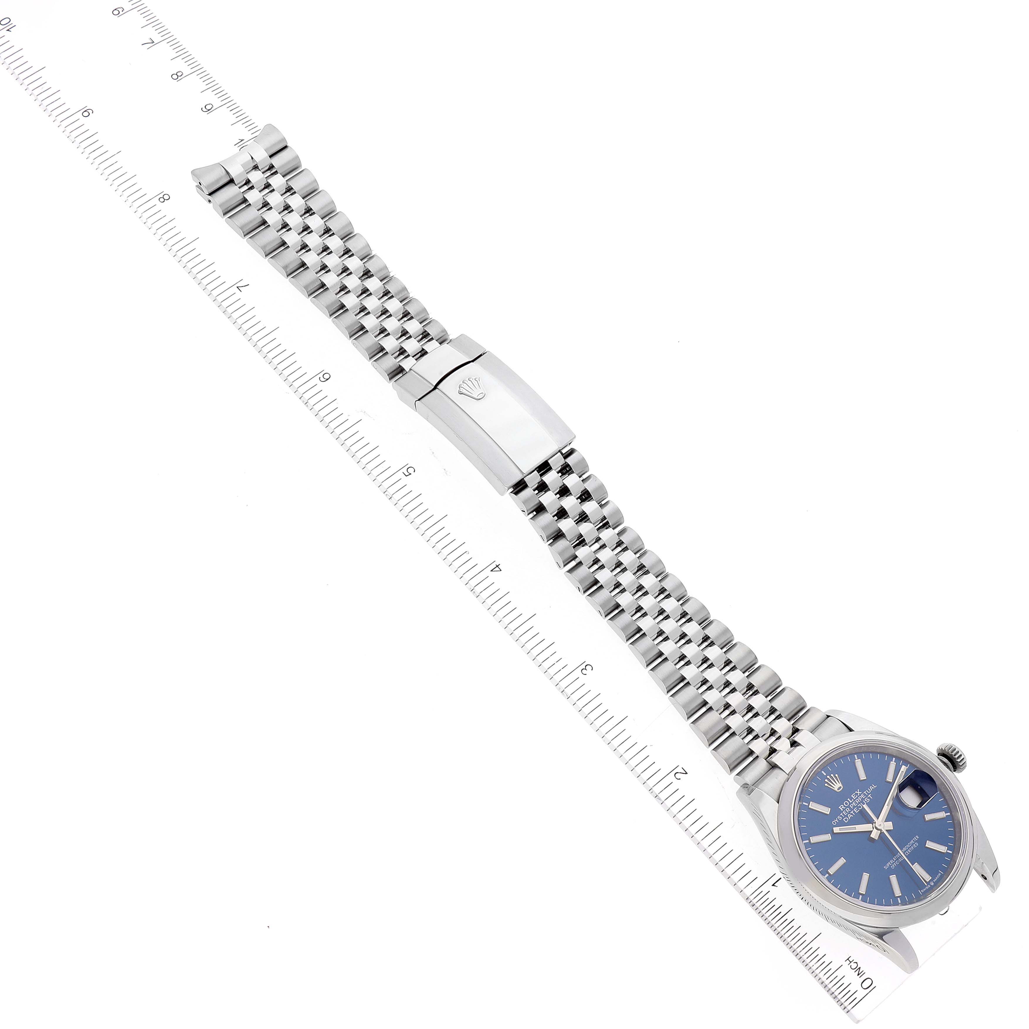 The image shows a Rolex Datejust 126200 Men's Stainless Steel Blue Dial 126200 Men's Stainless Steel Blue Dial watch laid flat with a ruler for scale, highlighting the bracelet and clasp.
