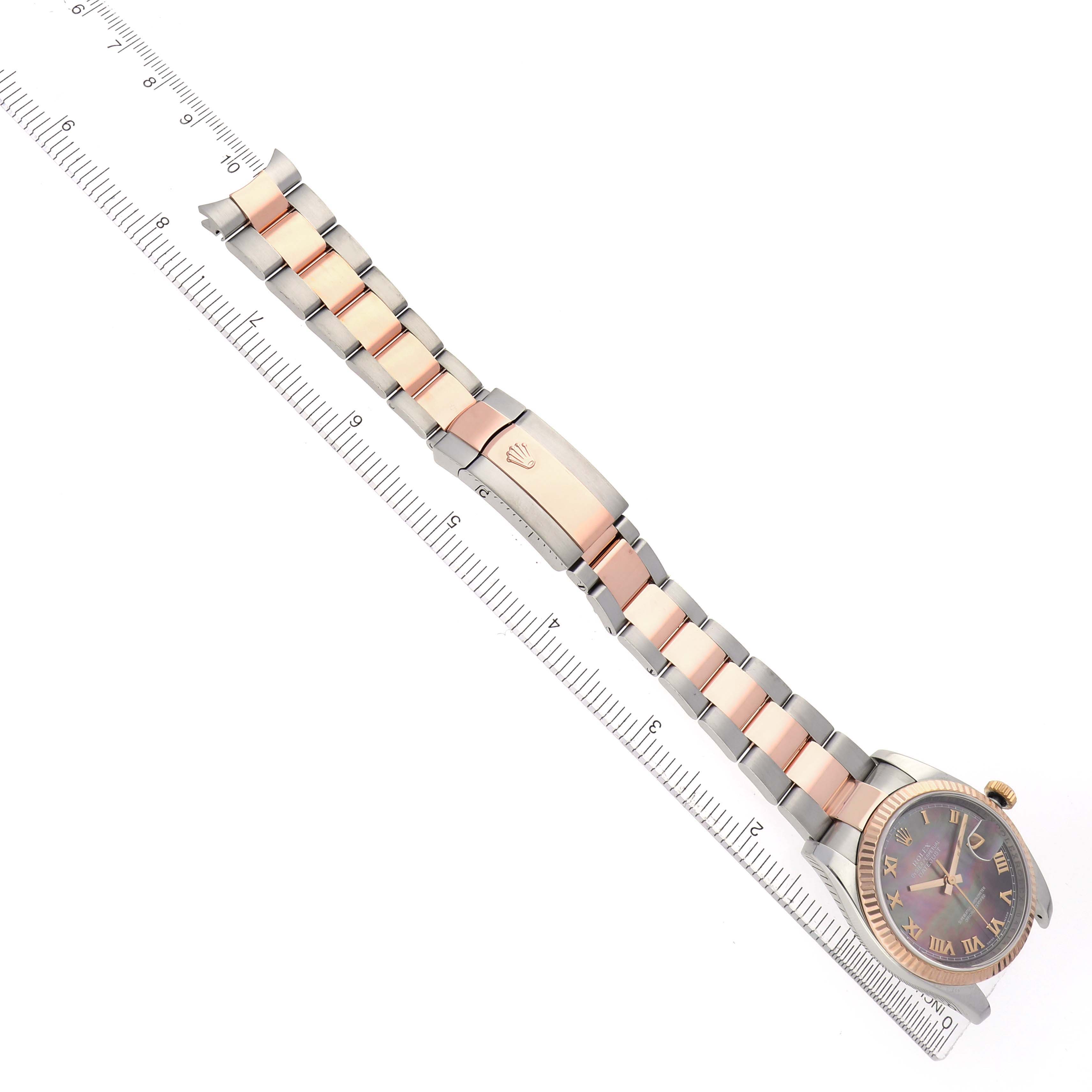 The Rolex Datejust 116231 Men
s Steel and Gold (two tone) Mother of Pearl Dial watch is shown at an angled top view with the full bracelet and clasp visible alongside a ruler.