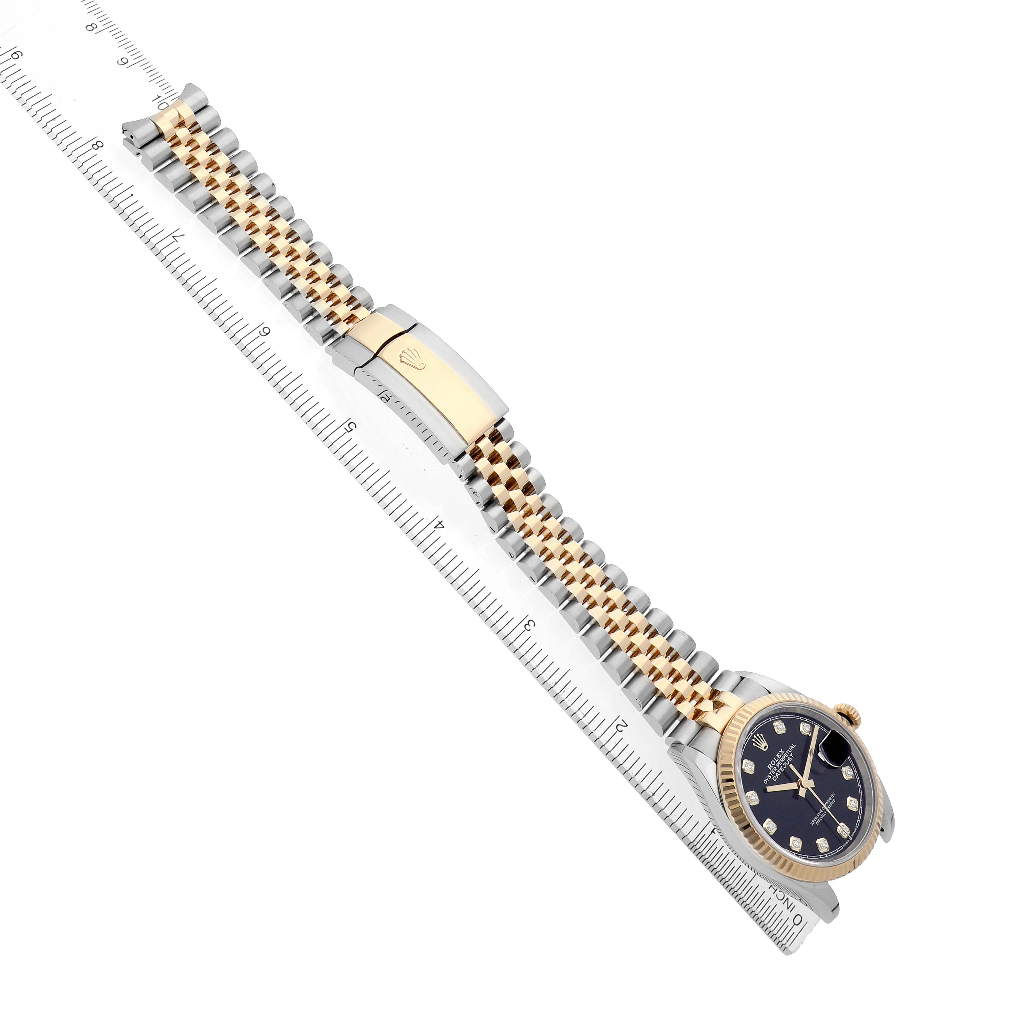 The image shows a Rolex Datejust 126233 Men
s Steel and Gold (two tone) Black Dial watch at an angle, highlighting its bracelet, clasp, and part of the dial next to a ruler.