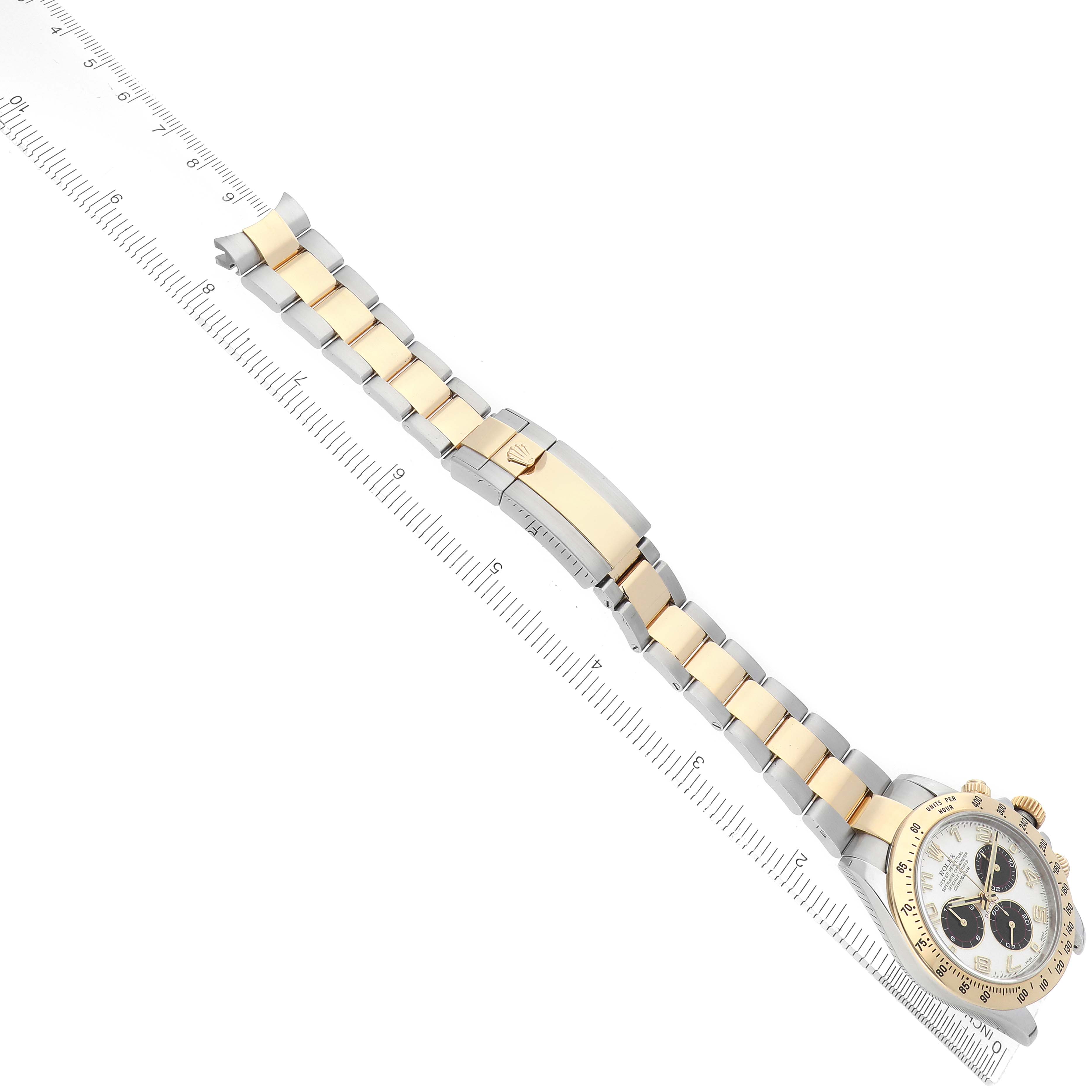 The Rolex Daytona 116523 Men
s Steel and Gold (two tone) White Dial watch is shown at an angled top view, highlighting its bracelet, clasp, and case with a ruler for scale.