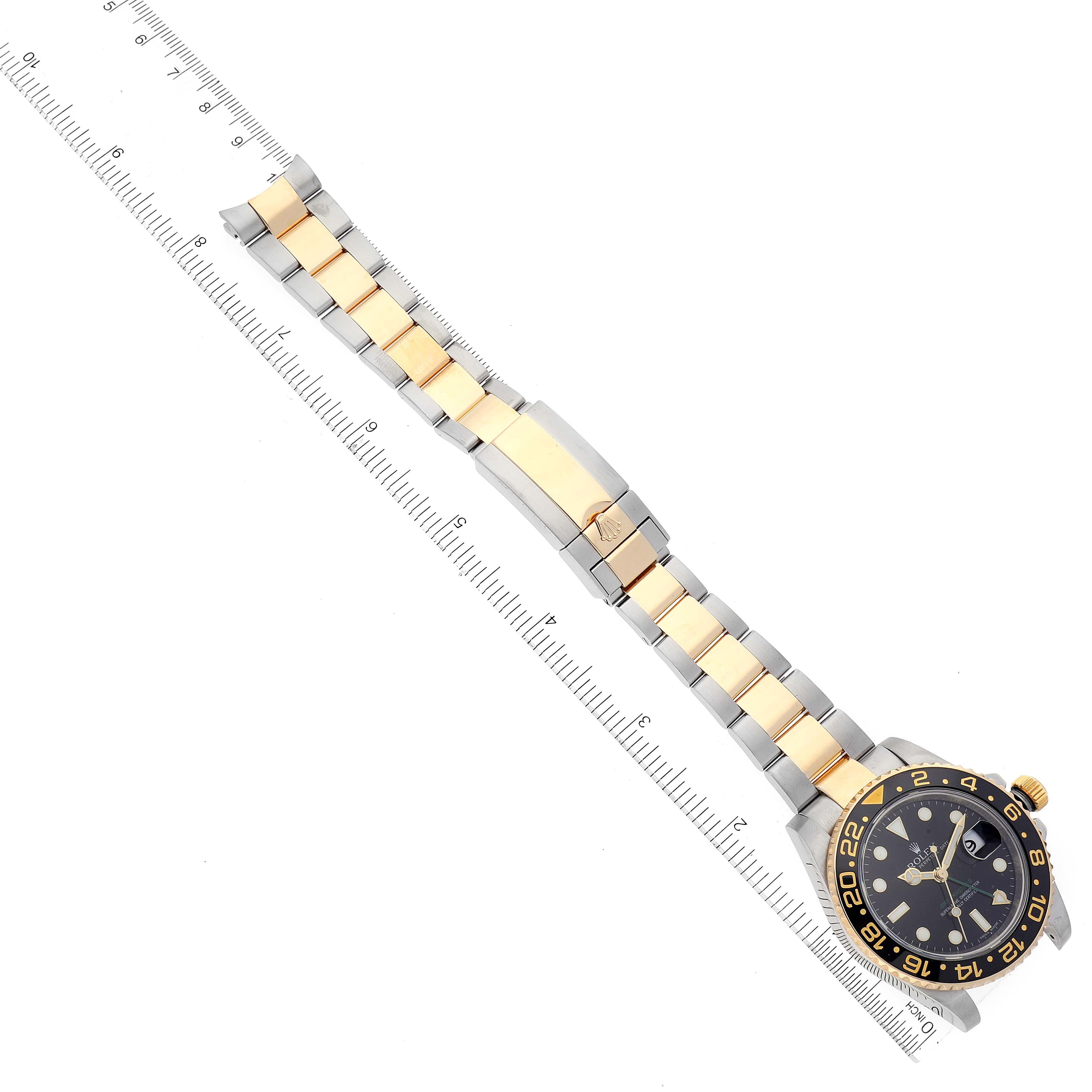 The image shows a top view of a Rolex GMT-Master 116713 Men's Steel and Gold (two tone) Black Dial 116713 Men's Steel and Gold (two tone) Black Dial watch, with a black and gold bezel and a gold and steel bracelet next to a ruler.