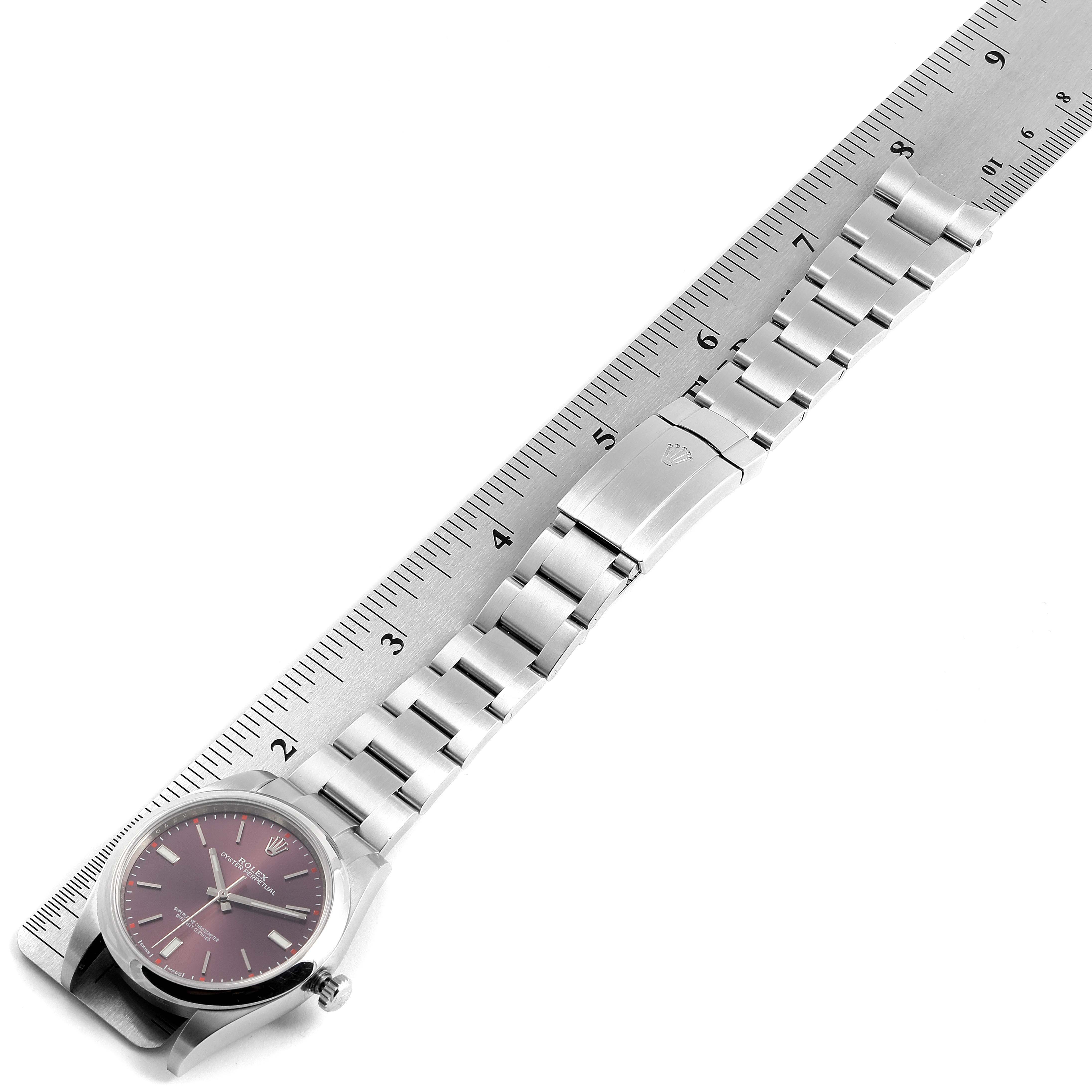 This image shows the Rolex Oyster Perpetual 114300 Men's Stainless Steel Burgundy Dial 114300 Men's Stainless Steel Burgundy Dial watch with its face and metal bracelet band alongside a ruler for measurement.