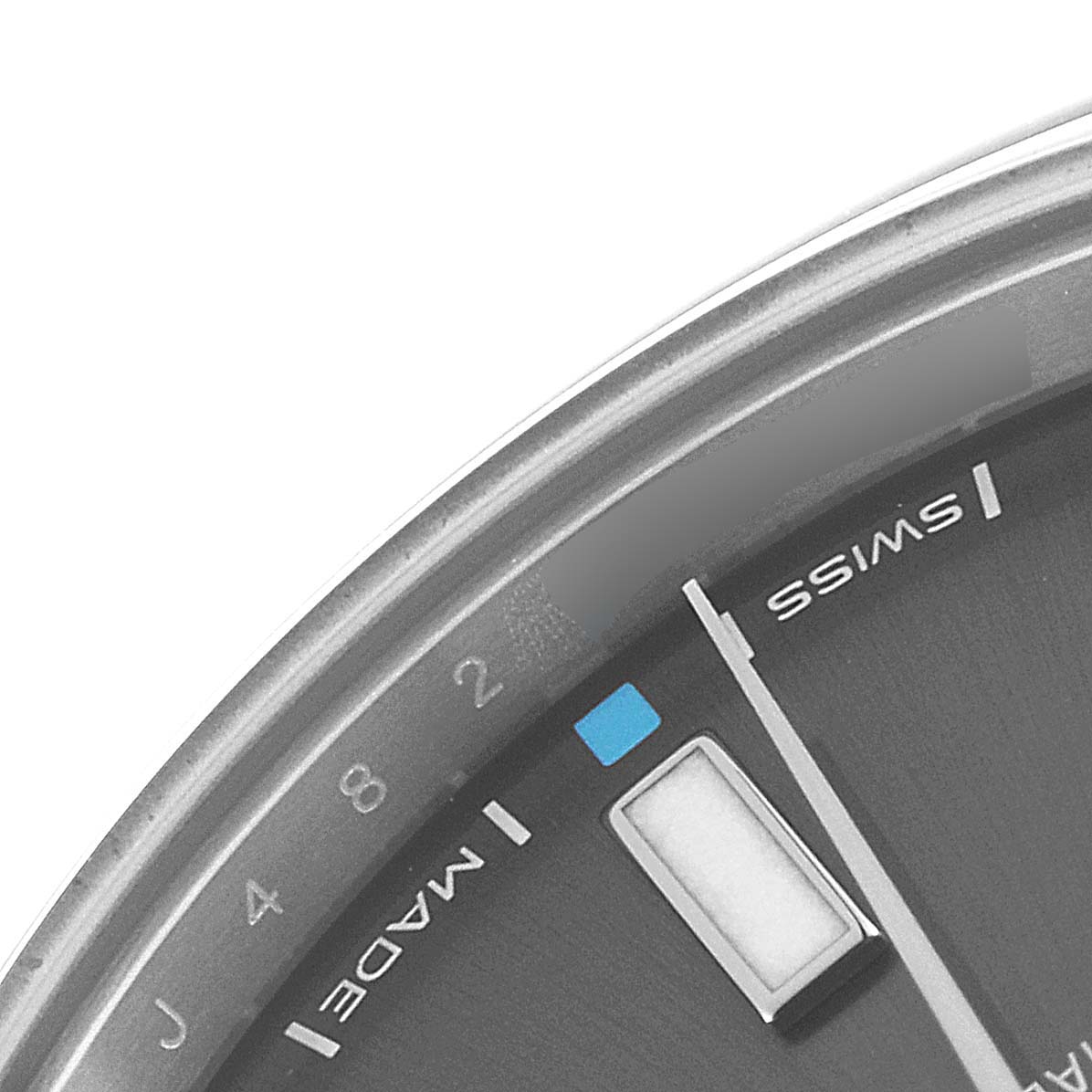 The image shows a close-up of the dial of a Rolex Oyster Perpetual 114300 Men
s Stainless Steel Silver Dial 114300 Men
s Stainless Steel Silver Dial watch, featuring part of the minute hand and indicators.