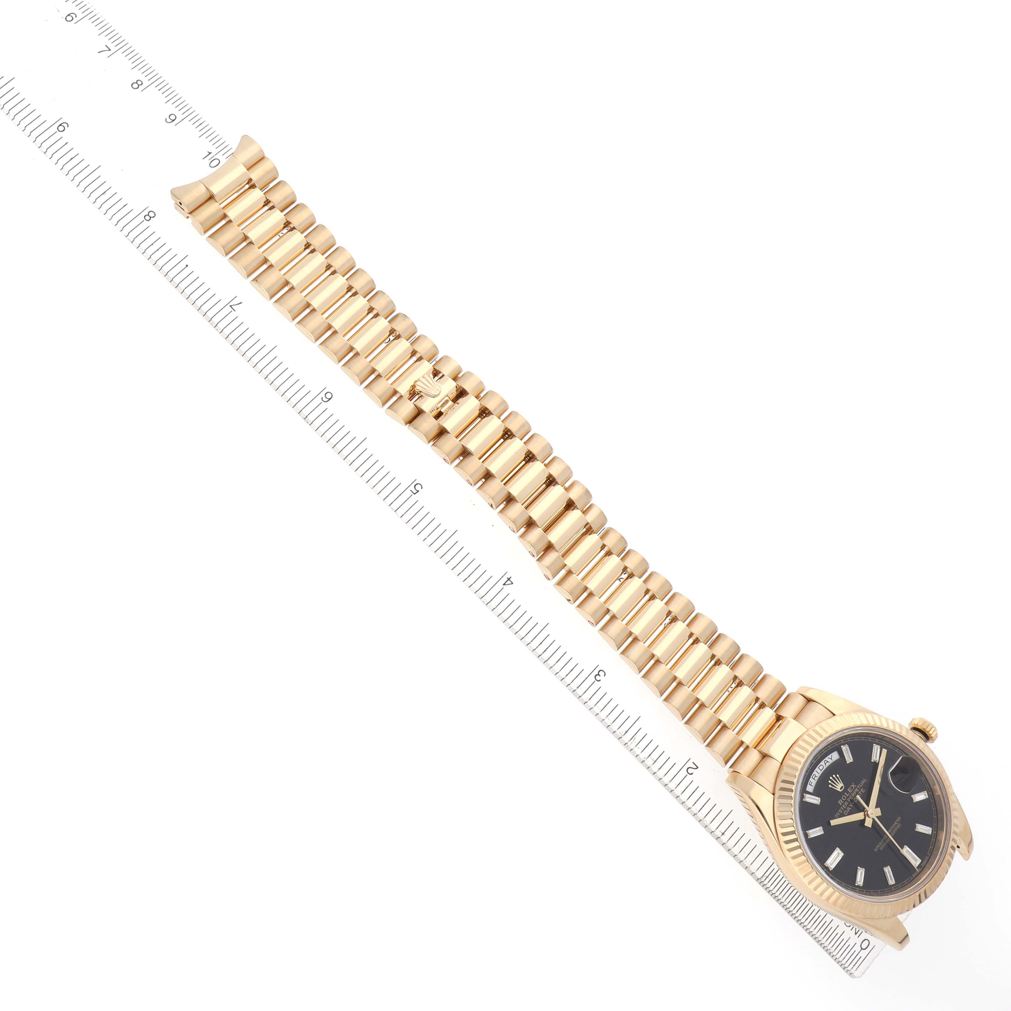 The Rolex President 228238 Men
s Yellow Gold Black Dial watch is shown at a slight top-down angle, displaying the case, bracelet, and part of the dial alongside a ruler.