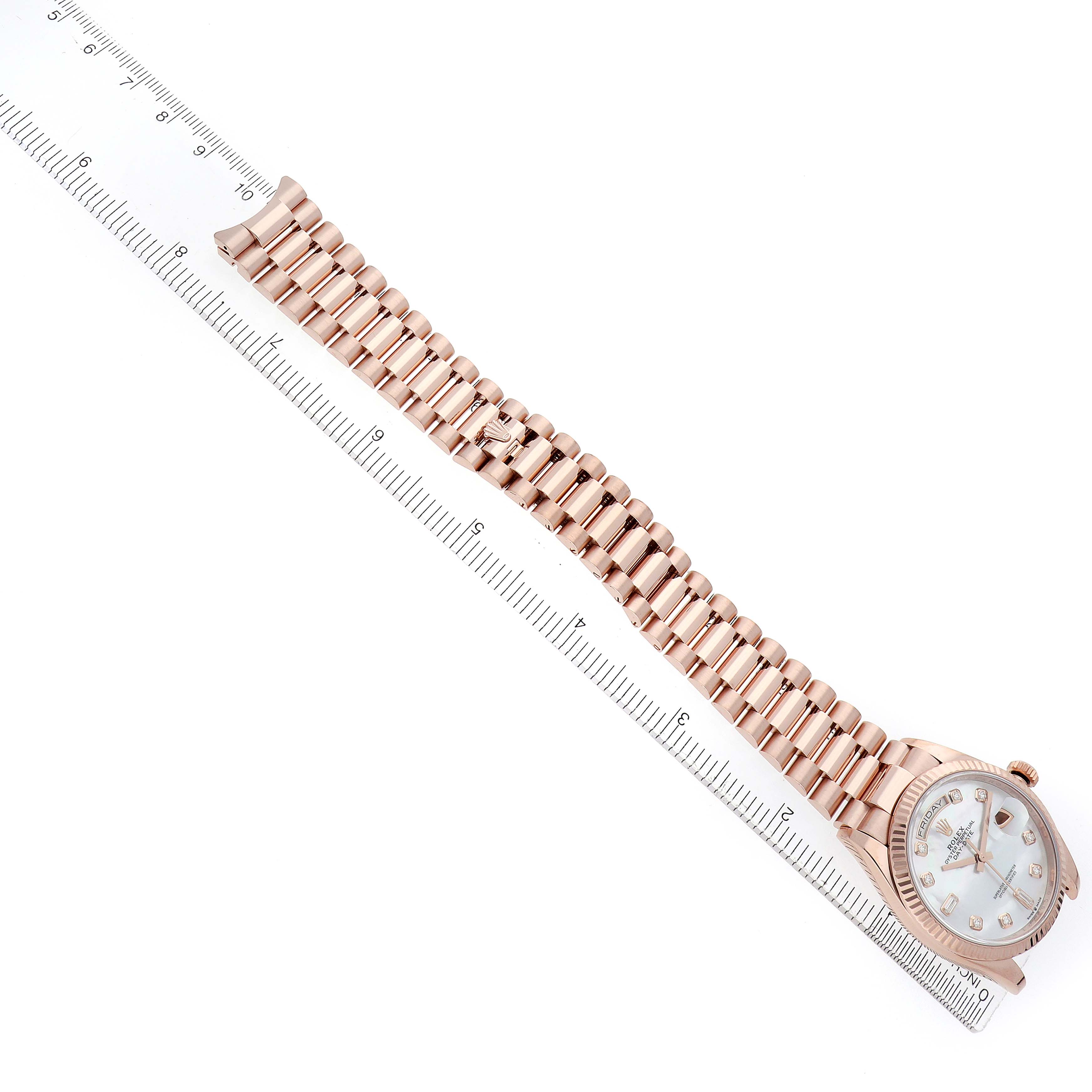 The Rolex President 128235 Men
s Rose Gold Mother of Pearl Dial watch is shown from a top-down angle, displaying the face and full bracelet alongside a ruler for scale.