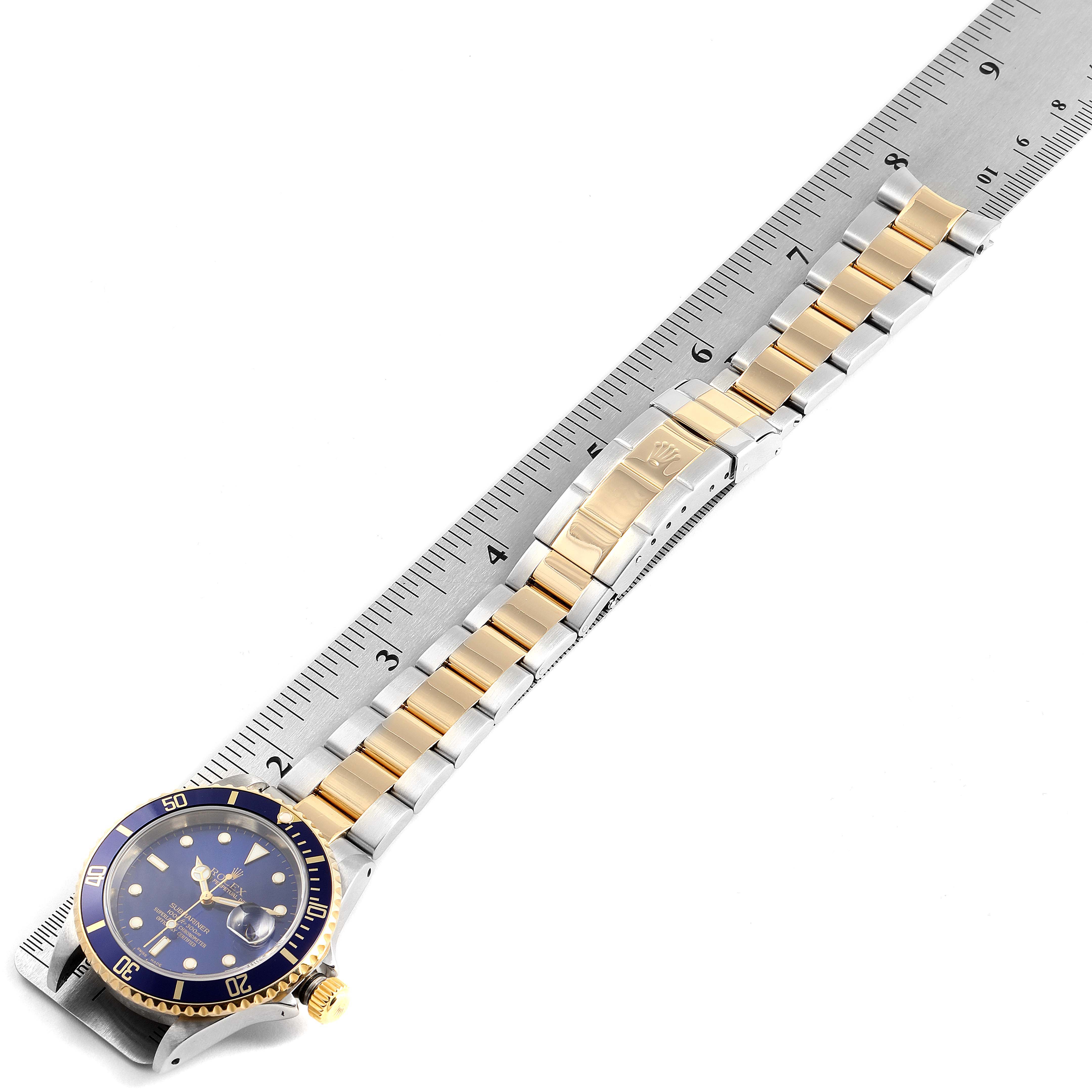 The image shows the Rolex Submariner 16613 Men's Steel and Gold (two tone) Blue Dial 16613 Men's Steel and Gold (two tone) Blue Dial watch from a top-down angle, displaying its face, dial, bezel, and full two-tone bracelet laid out alongside a ruler.