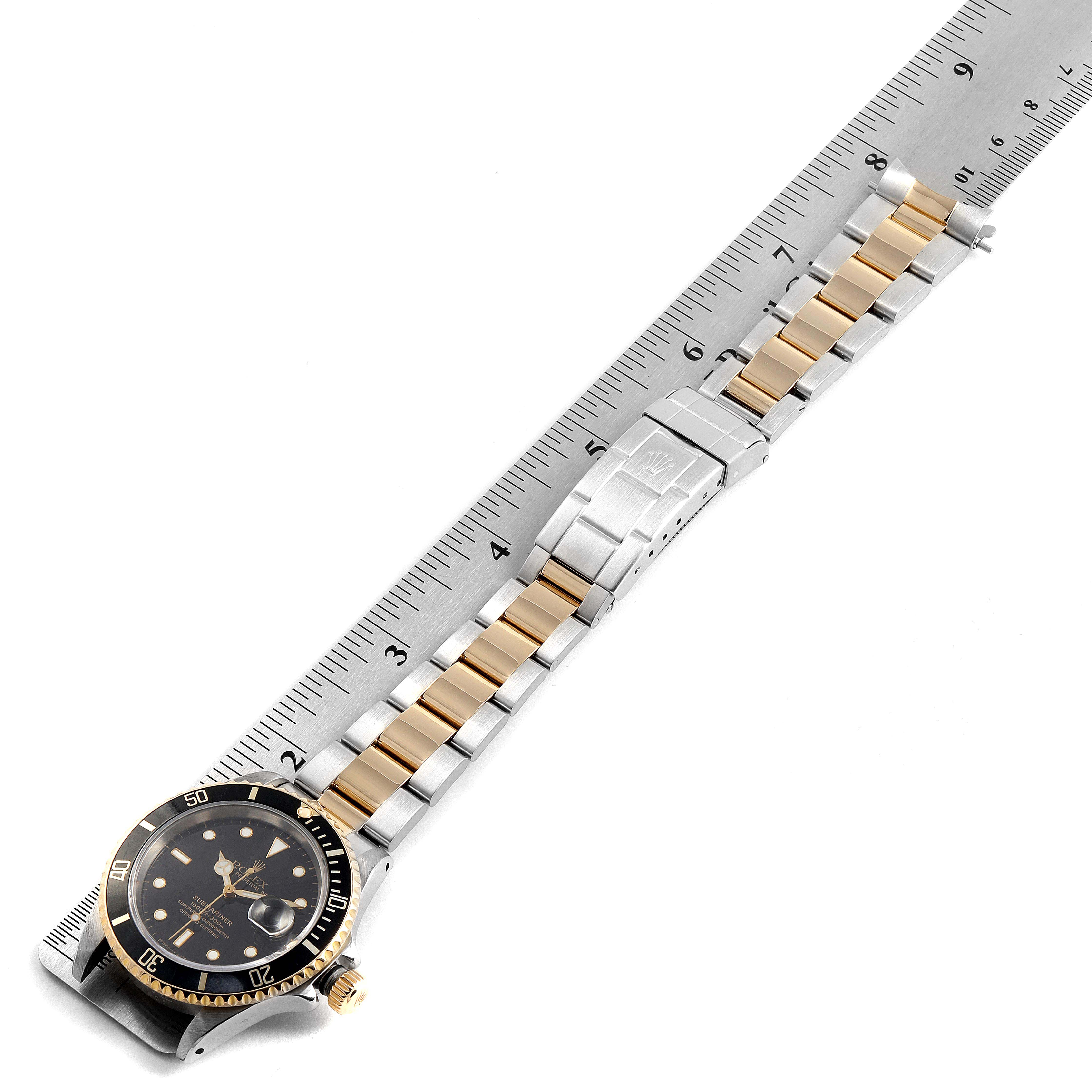 The image shows a Rolex Submariner 16613 Men's Steel and Gold (two tone) Black Dial 16613 Men's Steel and Gold (two tone) Black Dial watch laid flat with its bracelet extended next to a ruler for scale.