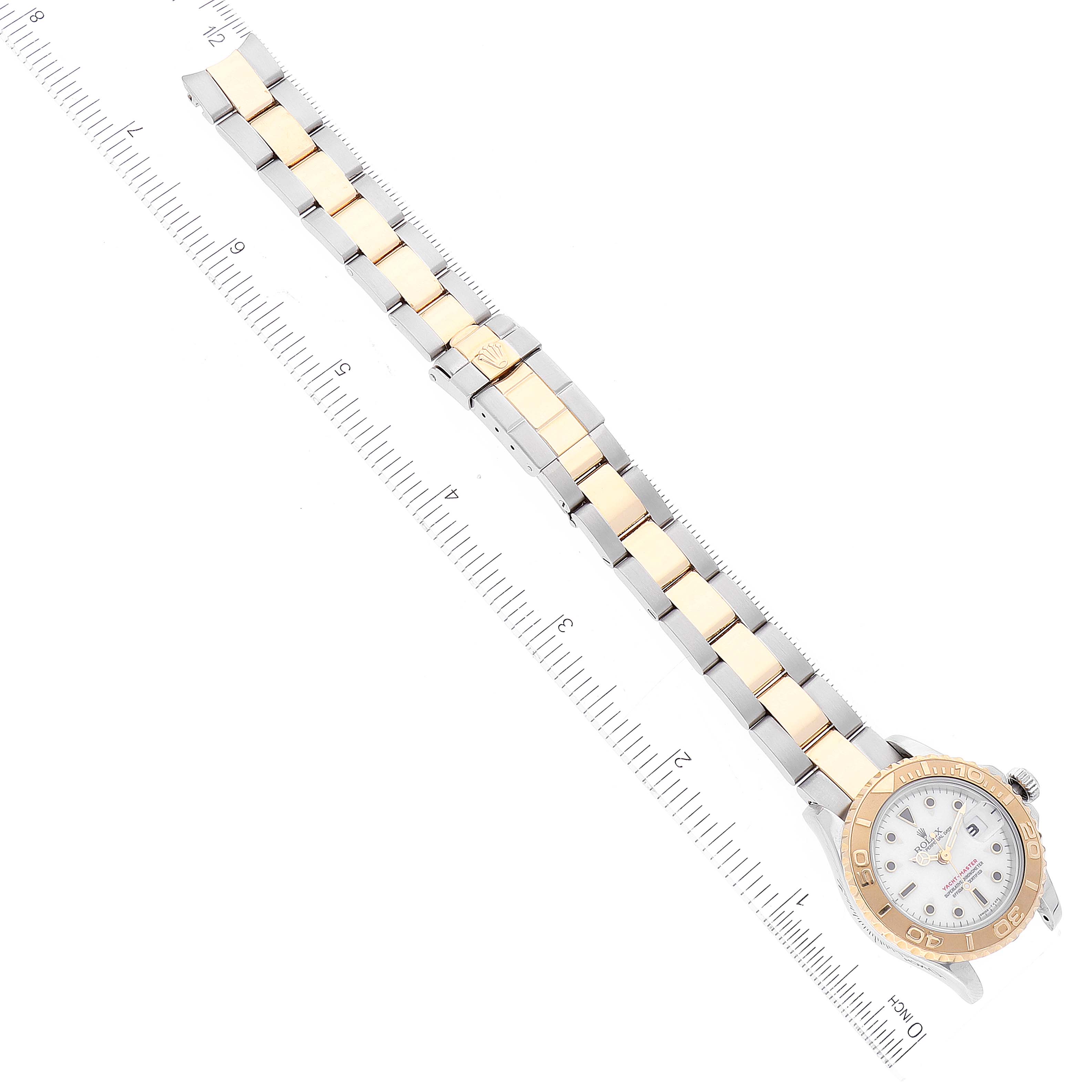 The image shows the Rolex Yacht-Master 69623 Women's Steel and Gold (two tone) White Dial 69623 Women's Steel and Gold (two tone) White Dial watch horizontally from an overhead view, displaying its face and metal bracelet alongside a ruler.