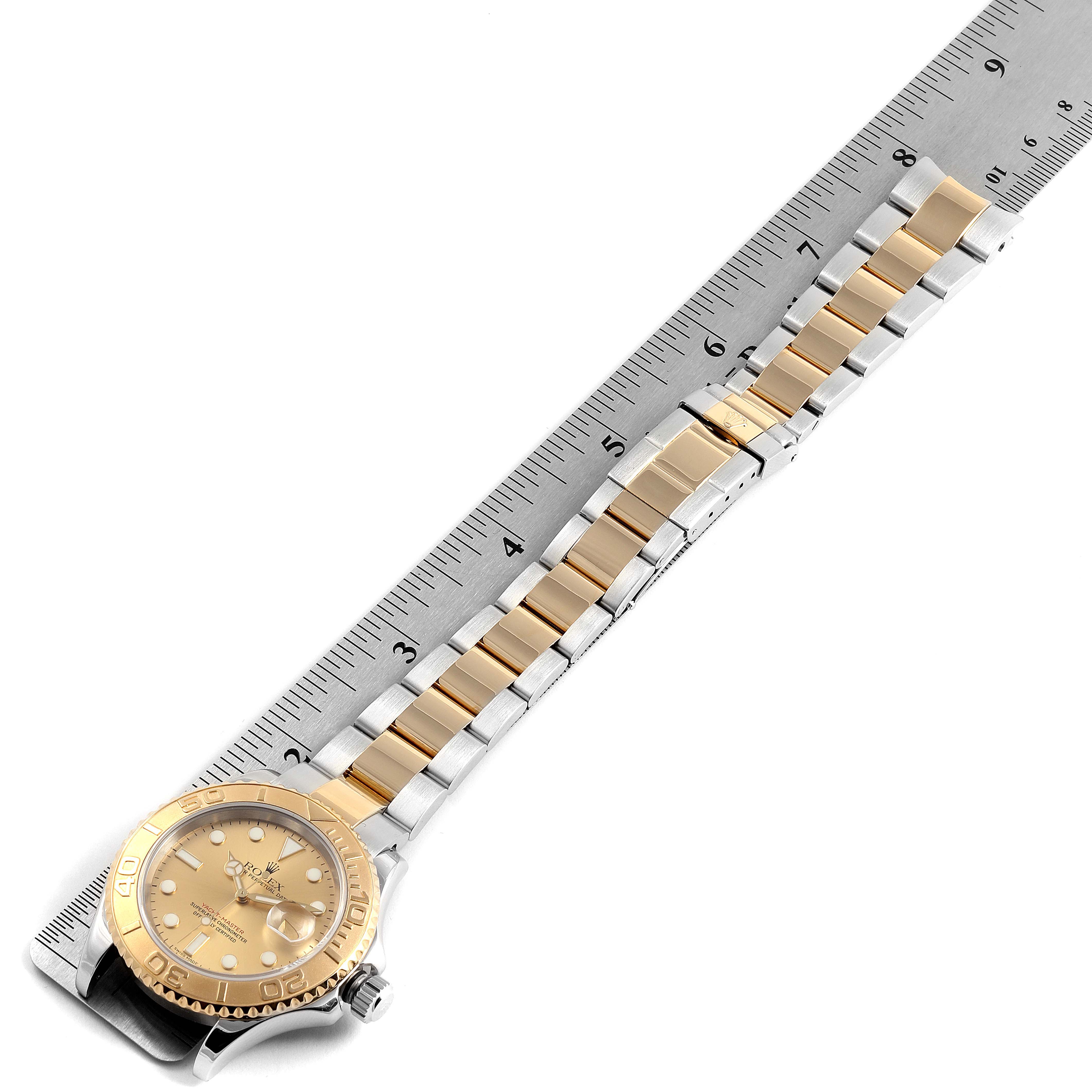 The Rolex Yacht-Master 16623 Men
s Steel and Gold (two tone) Champagne Dial 16623 Men
s Steel and Gold (two tone) Champagne Dial watch is shown from a top-down angle, displaying its face, bezel, and bracelet laid alongside a ruler.
