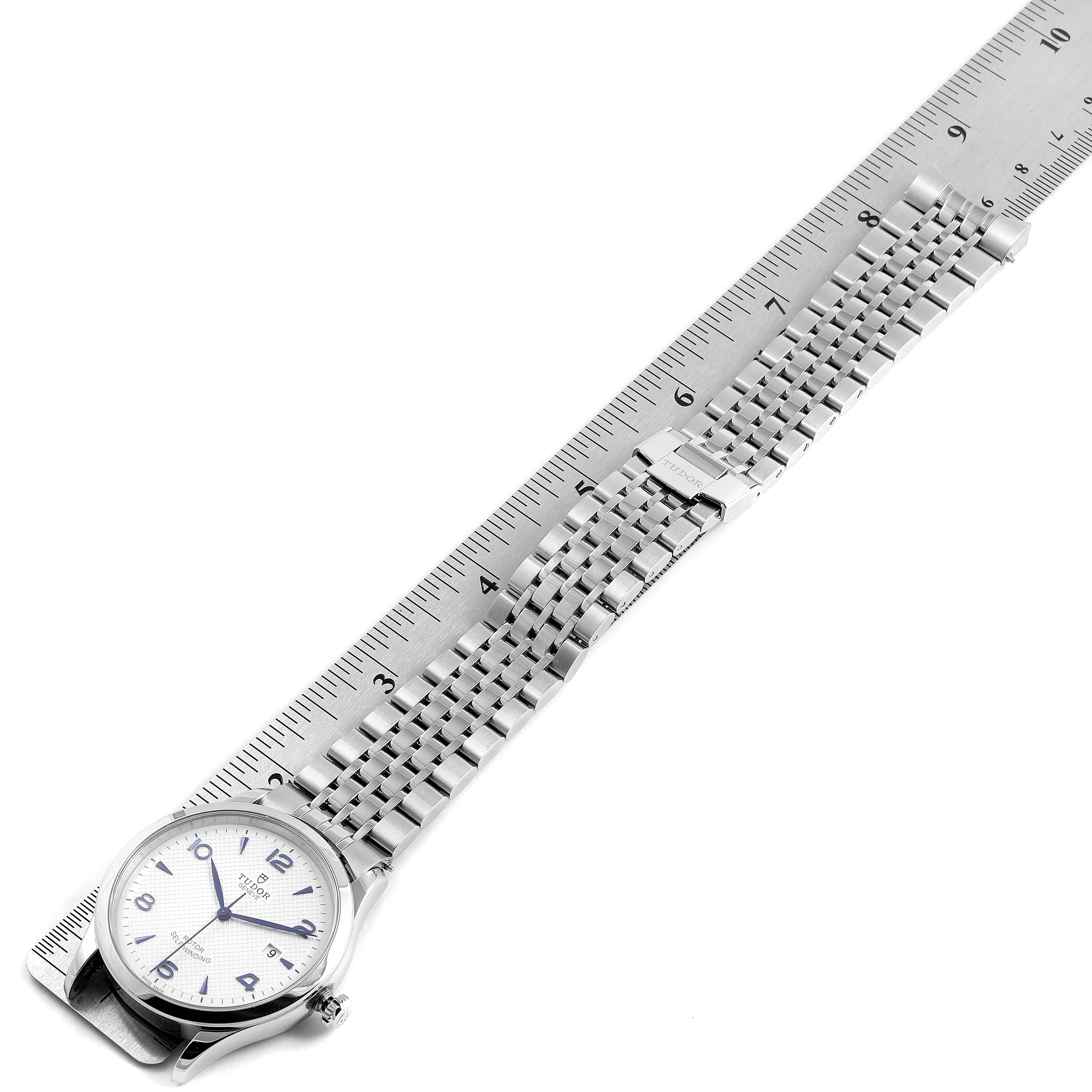 The image shows a Tudor 1926 M91650-0005 Men's Stainless Steel Silver Dial M91650-0005 Men's Stainless Steel Silver Dial model watch, photographed from above, lying next to a ruler displaying its stainless steel bracelet and clasp.