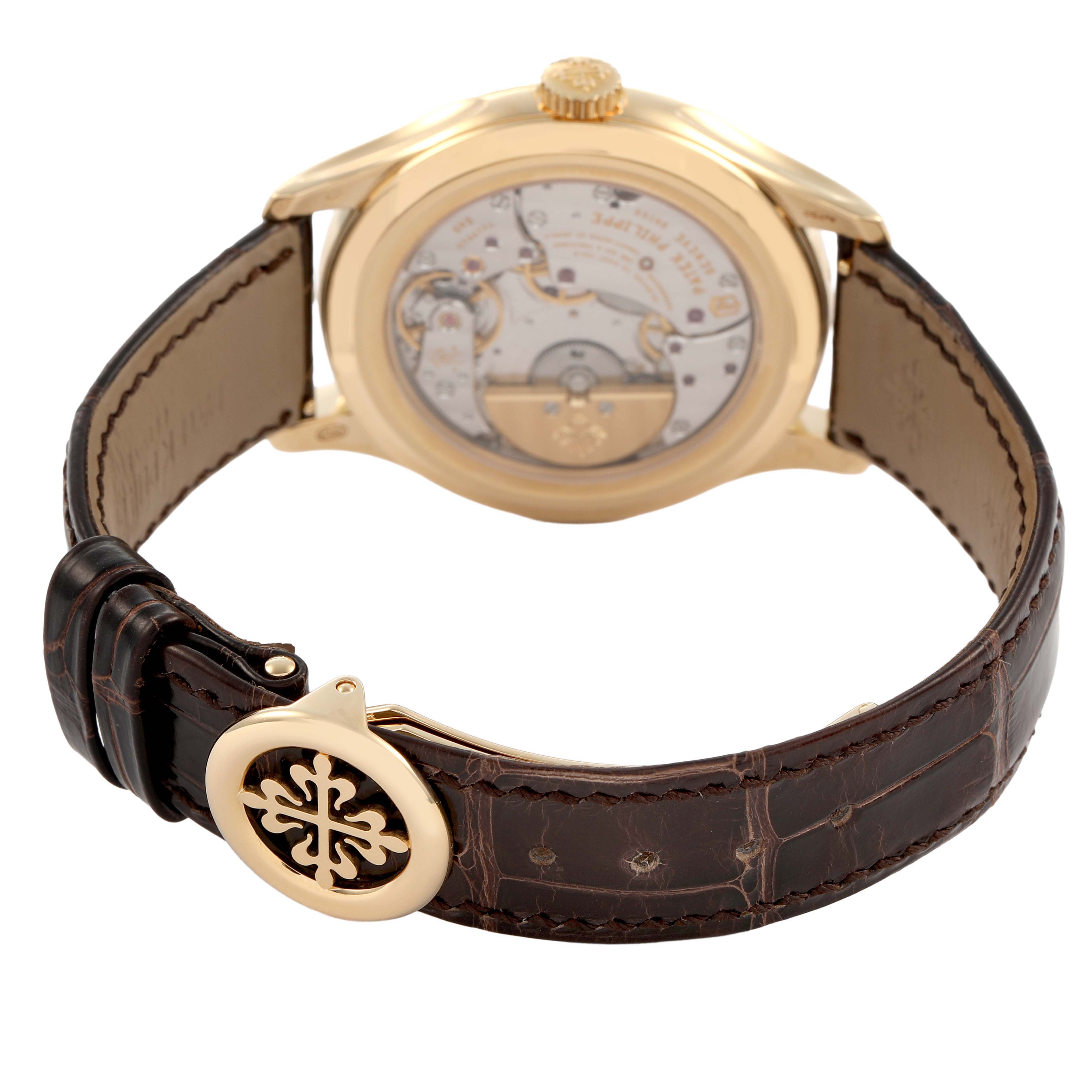 The image shows the back of the Patek Philippe Complications 5327J-001 Men's Yellow Gold Beige Dial watch, highlighting the movement and leather strap with the logo clasp.