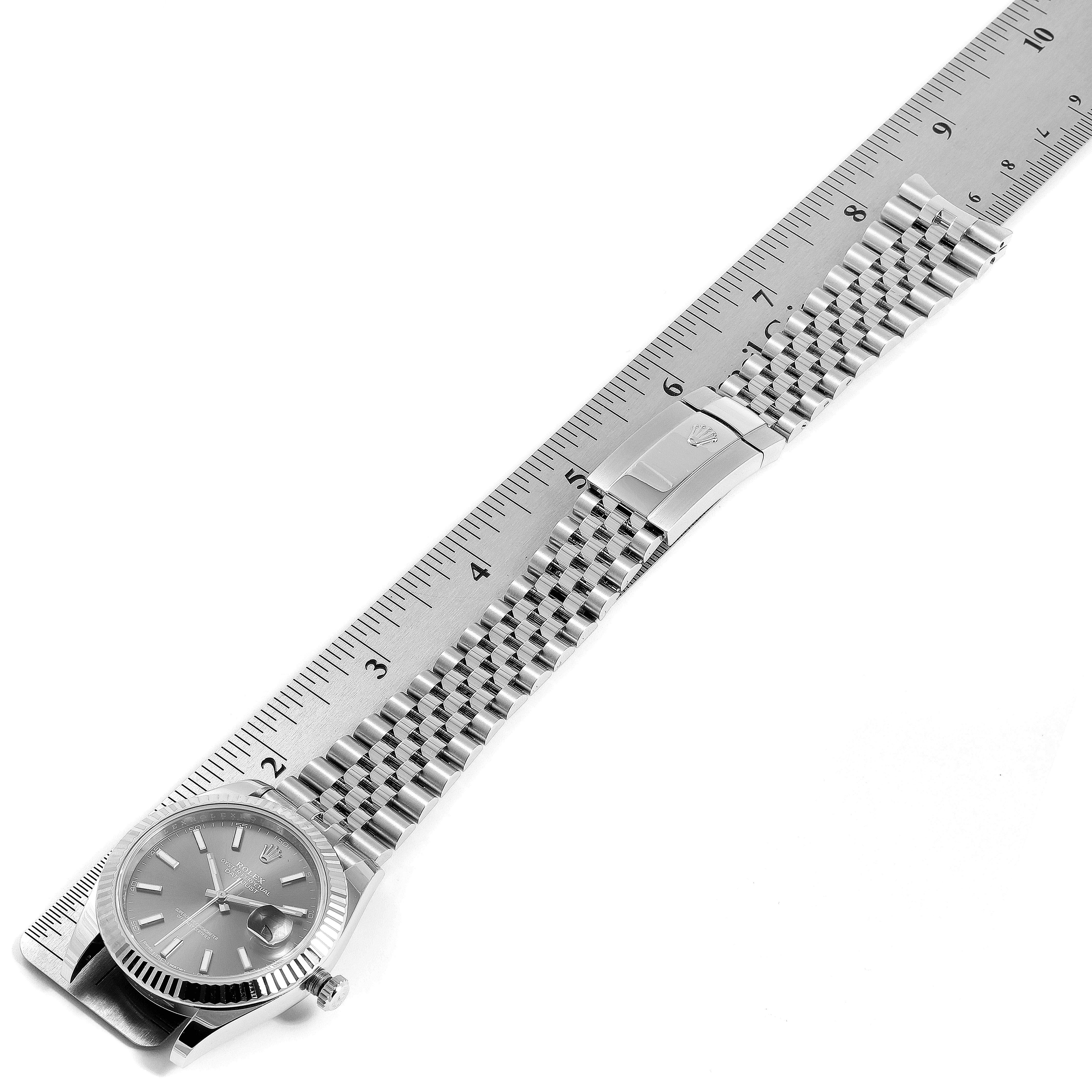 The image shows a Rolex Datejust 41 126334 Men
s Stainless Steel Grey Dial 126334 Men
s Stainless Steel Grey Dial watch laid flat with a metal ruler beside it, highlighting the face and bracelet with the clasp.