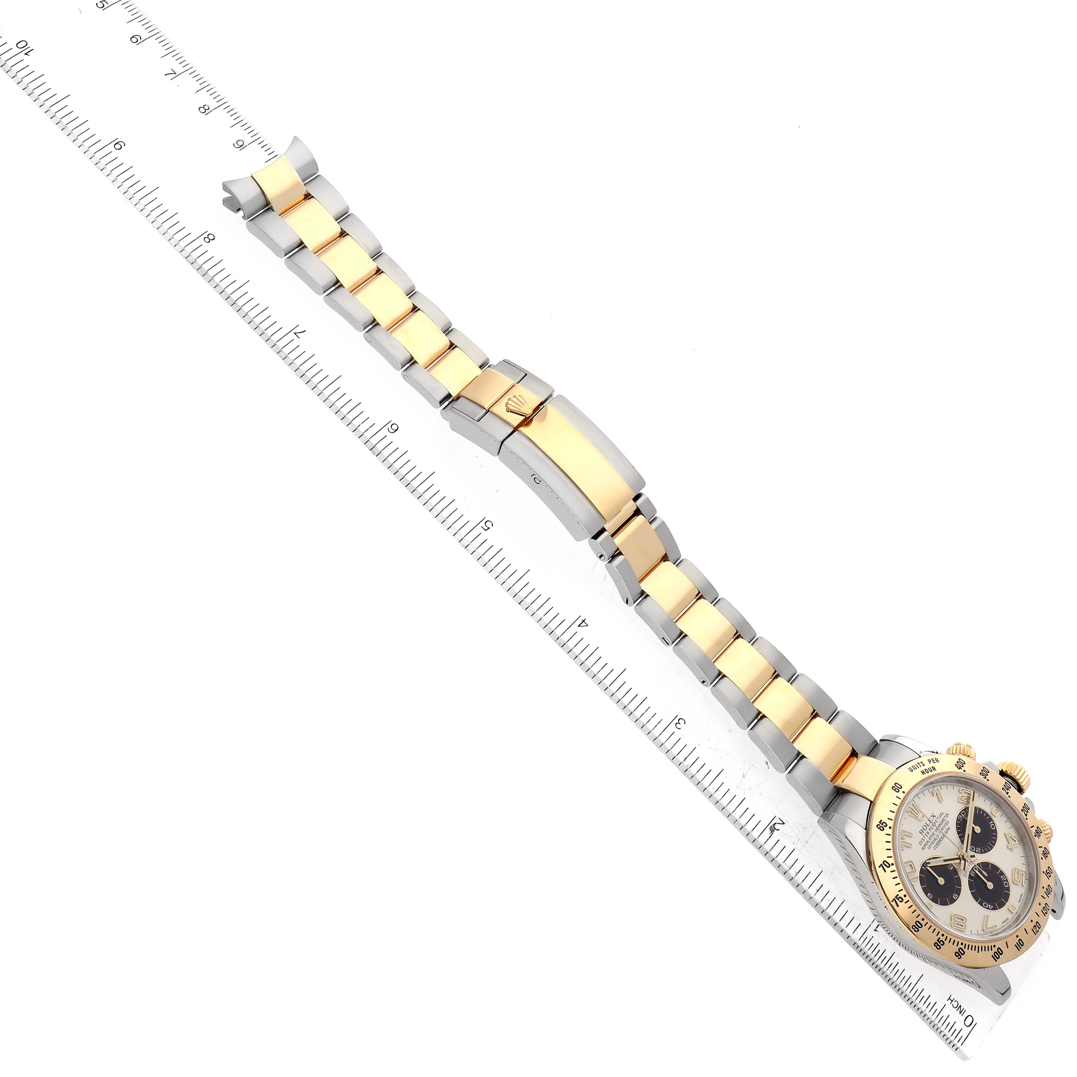 The image shows a top view of a Rolex Daytona 116523 Men's Steel and Gold (two tone) Silver Dial 116523 Men's Steel and Gold (two tone) Silver Dial watch, featuring its metal bracelet and clasp, alongside a measuring scale.