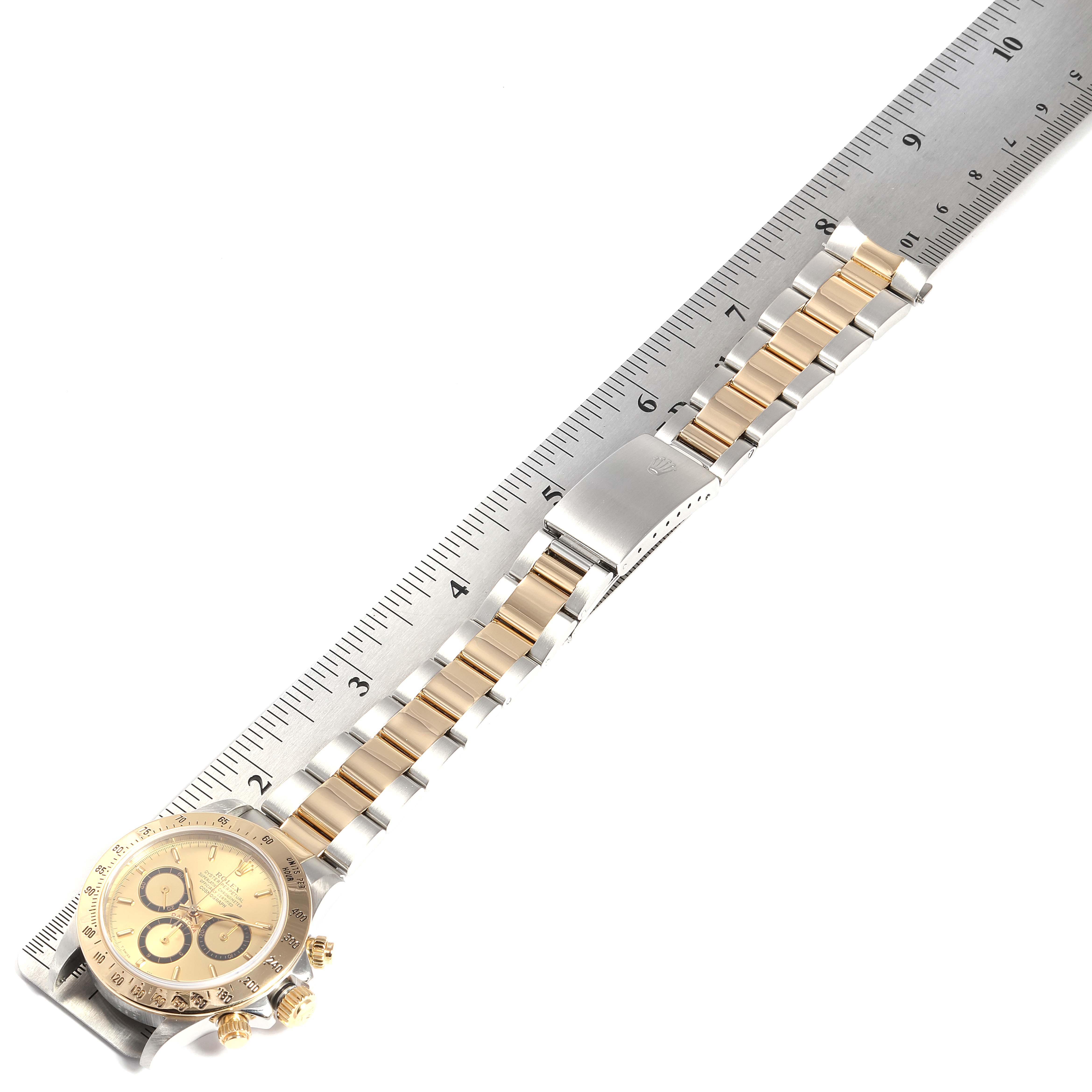 The image shows a Rolex Daytona 16523 Men's Steel and Gold (two tone) Champagne Dial 16523 Men's Steel and Gold (two tone) Champagne Dial watch laid flat next to a ruler, focusing on the bracelet and face.