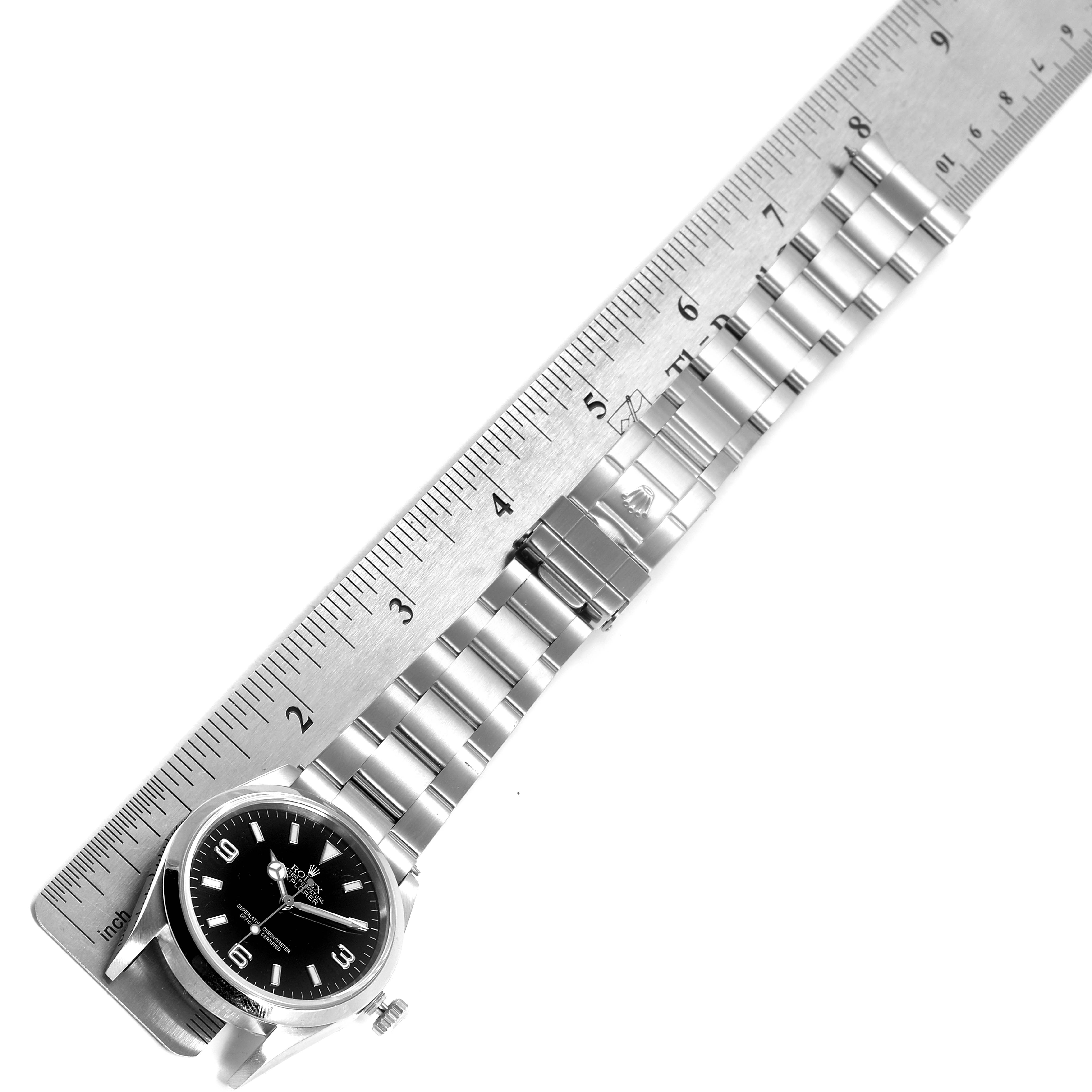 The image shows a top view of a Rolex Explorer 114270 Men
s Stainless Steel Black Dial 114270 Men
s Stainless Steel Black Dial watch next to a ruler, focusing on the bracelet and dial.