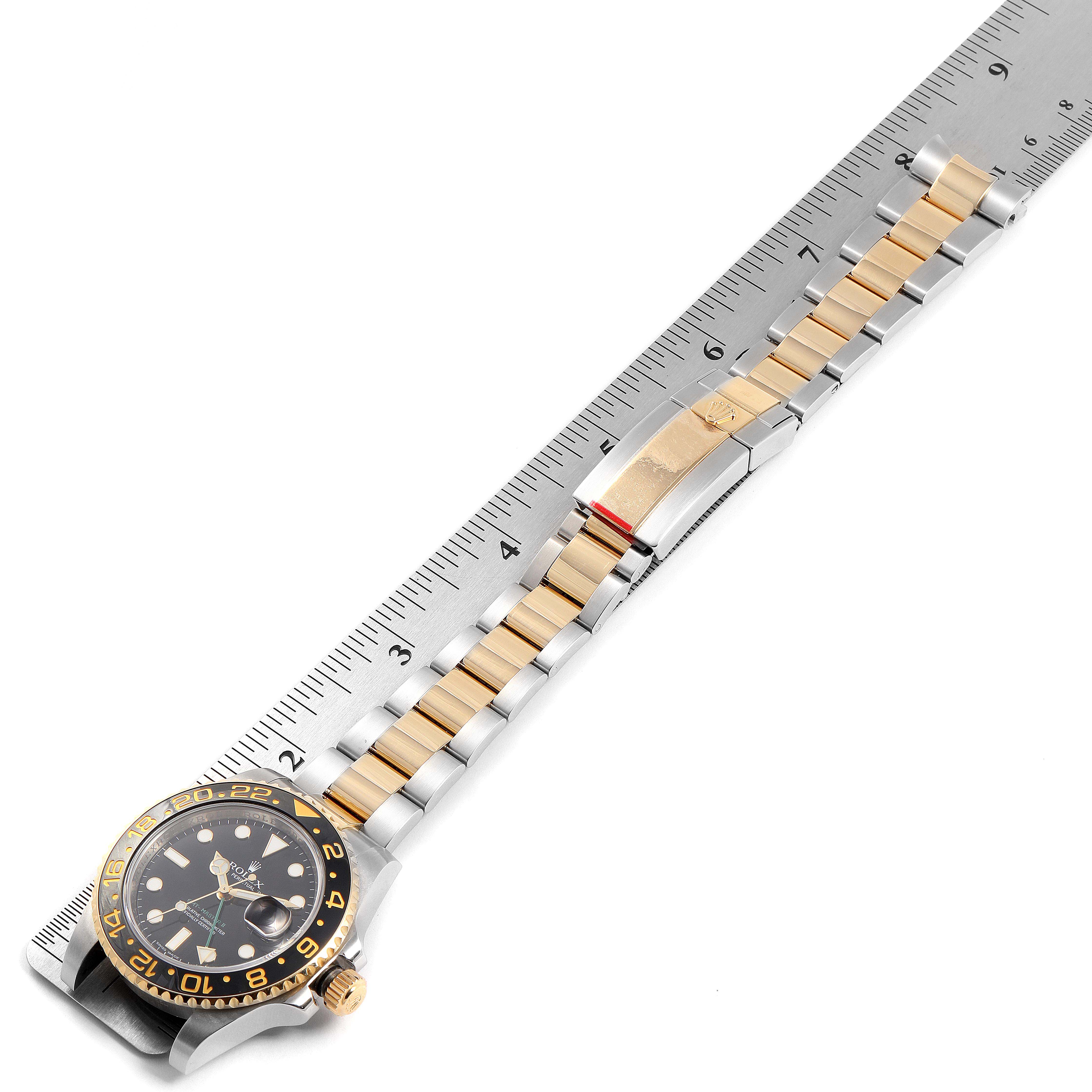 This image shows a Rolex GMT-Master 116713 Men's Steel and Gold (two tone) Black Dial 116713 Men's Steel and Gold (two tone) Black Dial watch laid flat with its face, bezel, and bracelet visible along a ruler for scale.