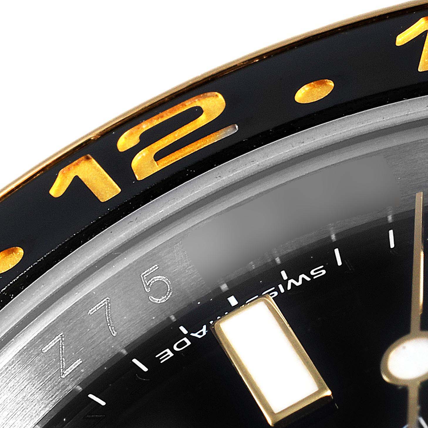 This close-up image of the Rolex GMT-Master 116713 Men's Steel and Gold (two tone) Black Dial 116713 Men's Steel and Gold (two tone) Black Dial watch shows the bezel with the number "12," part of the dial, and watch hands.