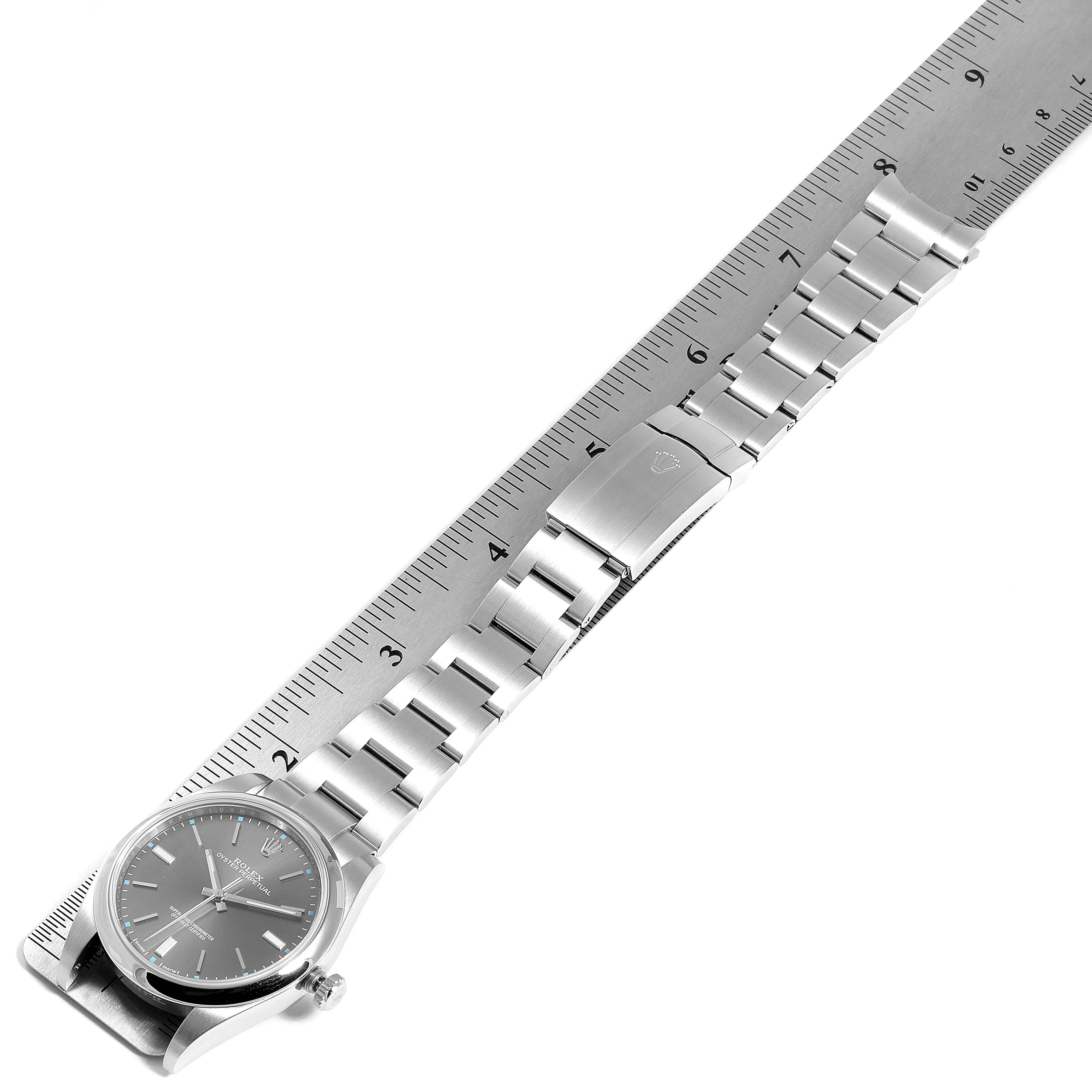 The Rolex Oyster Perpetual 114300 Men's Stainless Steel Silver Dial 114300 Men's Stainless Steel Silver Dial watch is shown from an angled top view, displaying its dial, bracelet, and deployment clasp against a ruler for measurement.