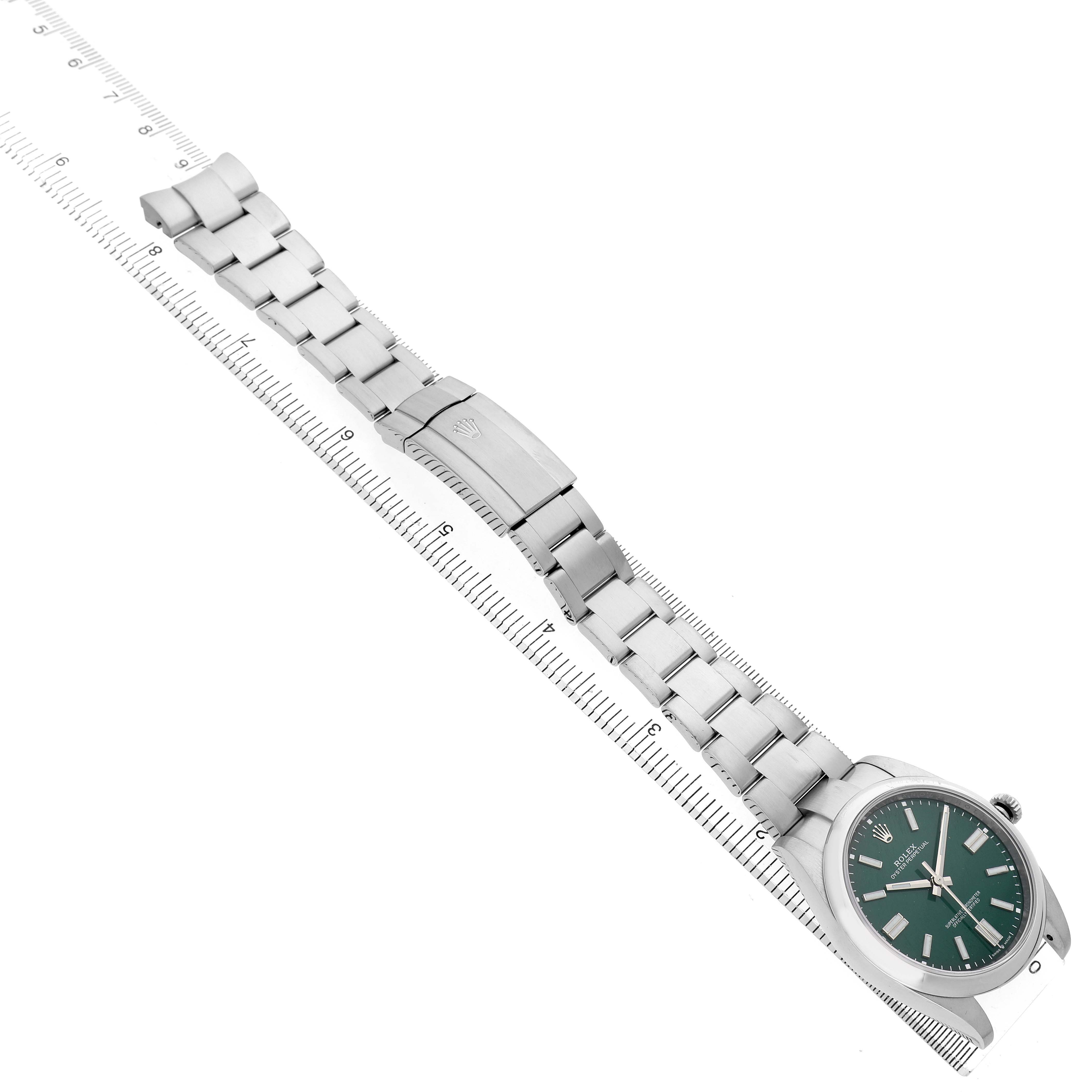 The image shows a Rolex Oyster Perpetual 124300 Men's Stainless Steel Green Dial watch laid flat, highlighting the bracelet and face against a ruler.