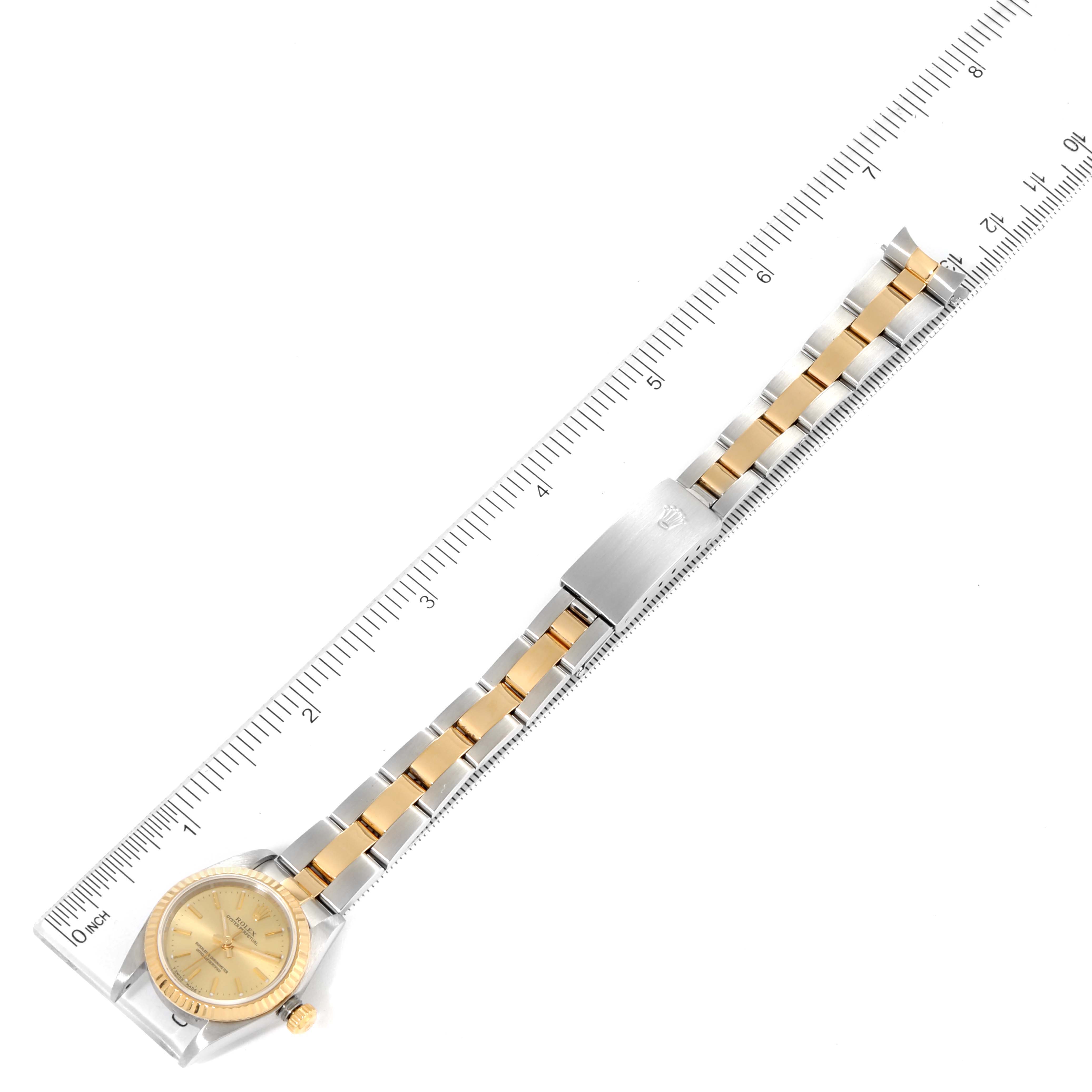 The image shows a top view of a Rolex Oyster Perpetual 76193 Women's Steel and Gold (two tone) Champagne Dial 76193 Women's Steel and Gold (two tone) Champagne Dial watch, highlighting the face, bezel, and bracelet in comparison to a ruler.