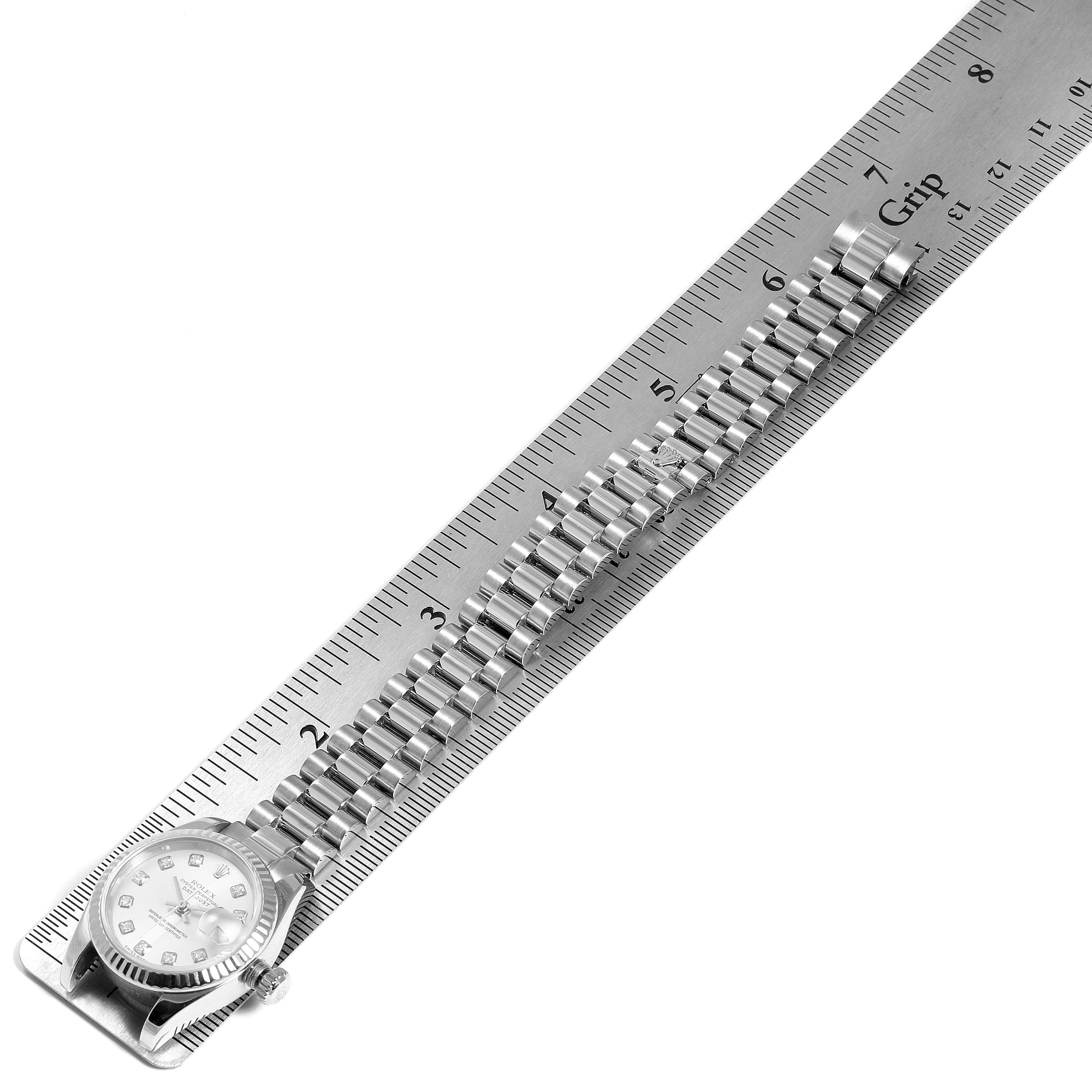 The image shows a Rolex President 179179 Women
s White Gold Silver Dial 179179 Women
s White Gold Silver Dial model watch placed alongside a ruler, highlighting its bracelet and face from a top-view angle.
