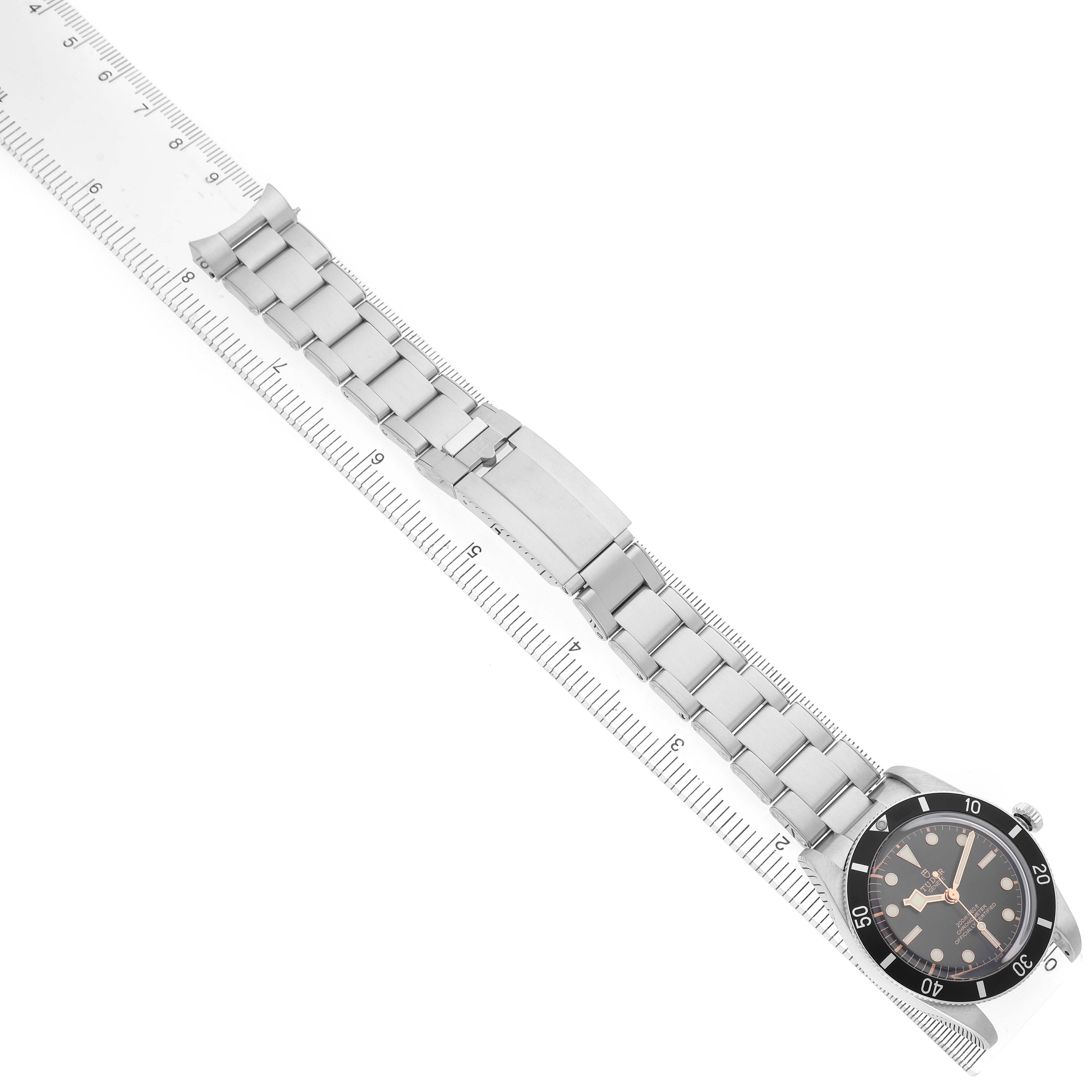 The image shows a top-down view of the Tudor Heritage Black Bay M79000N-0002 Men's Stainless Steel Black Dial watch with its full bracelet and clasp laid alongside a ruler.