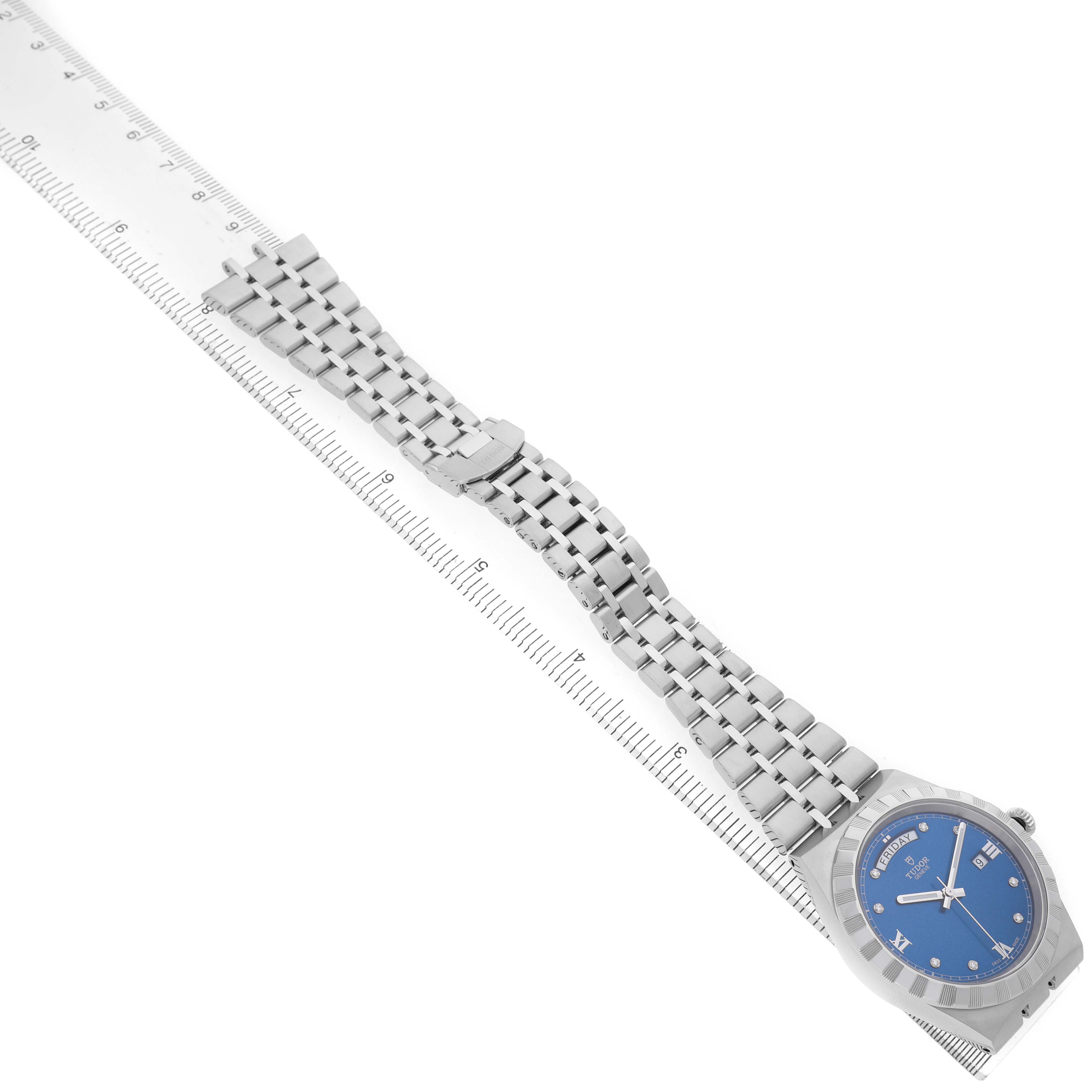 The Tudor Royal 28600 Men's Stainless Steel Blue Dial watch is photographed from an angled top view, showing the blue dial and metal bracelet alongside a ruler.
