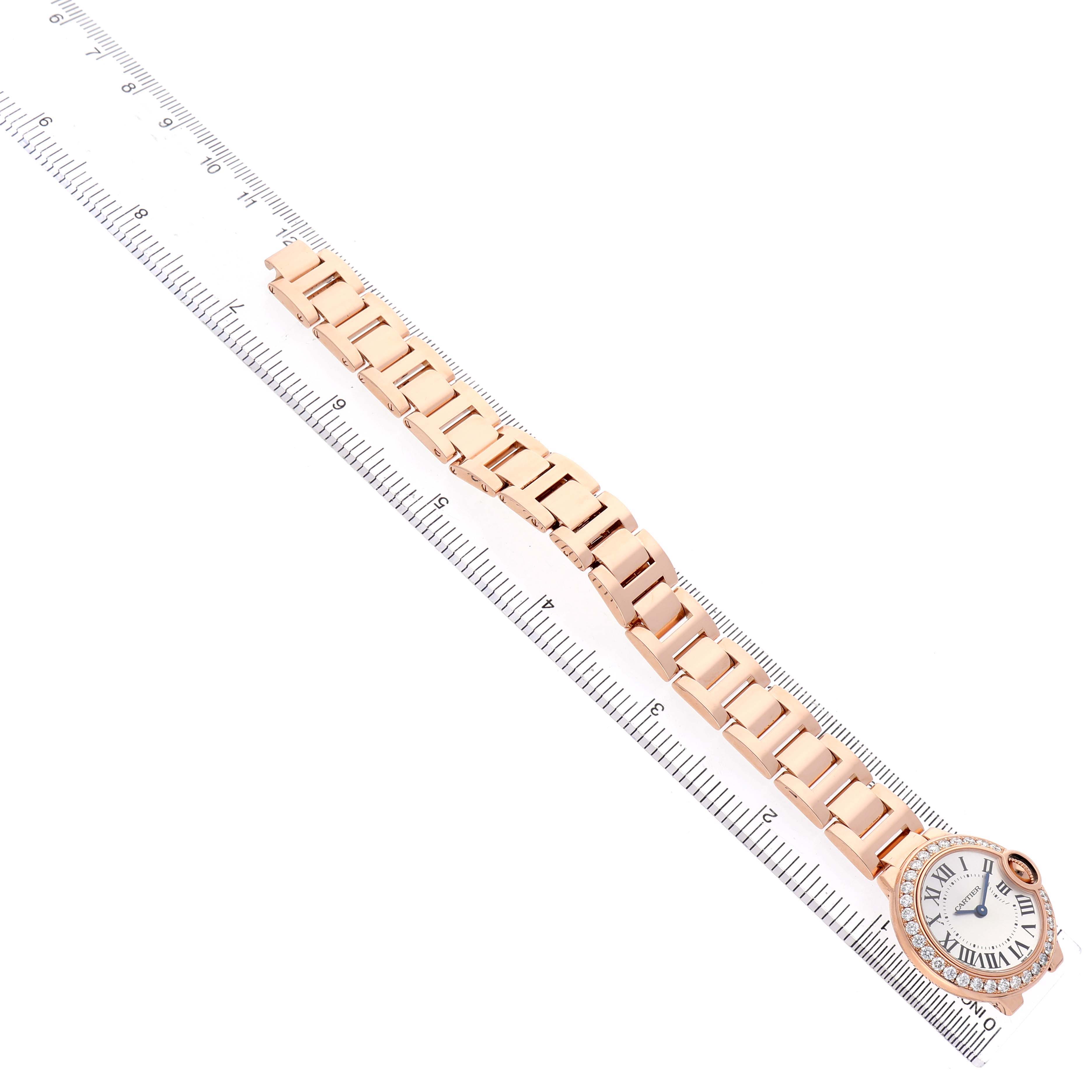 The Cartier Ballon Bleu WE9002Z3 Women's Rose Gold Silver Dial watch is shown from a top view, featuring the full bracelet and face placed alongside a ruler.