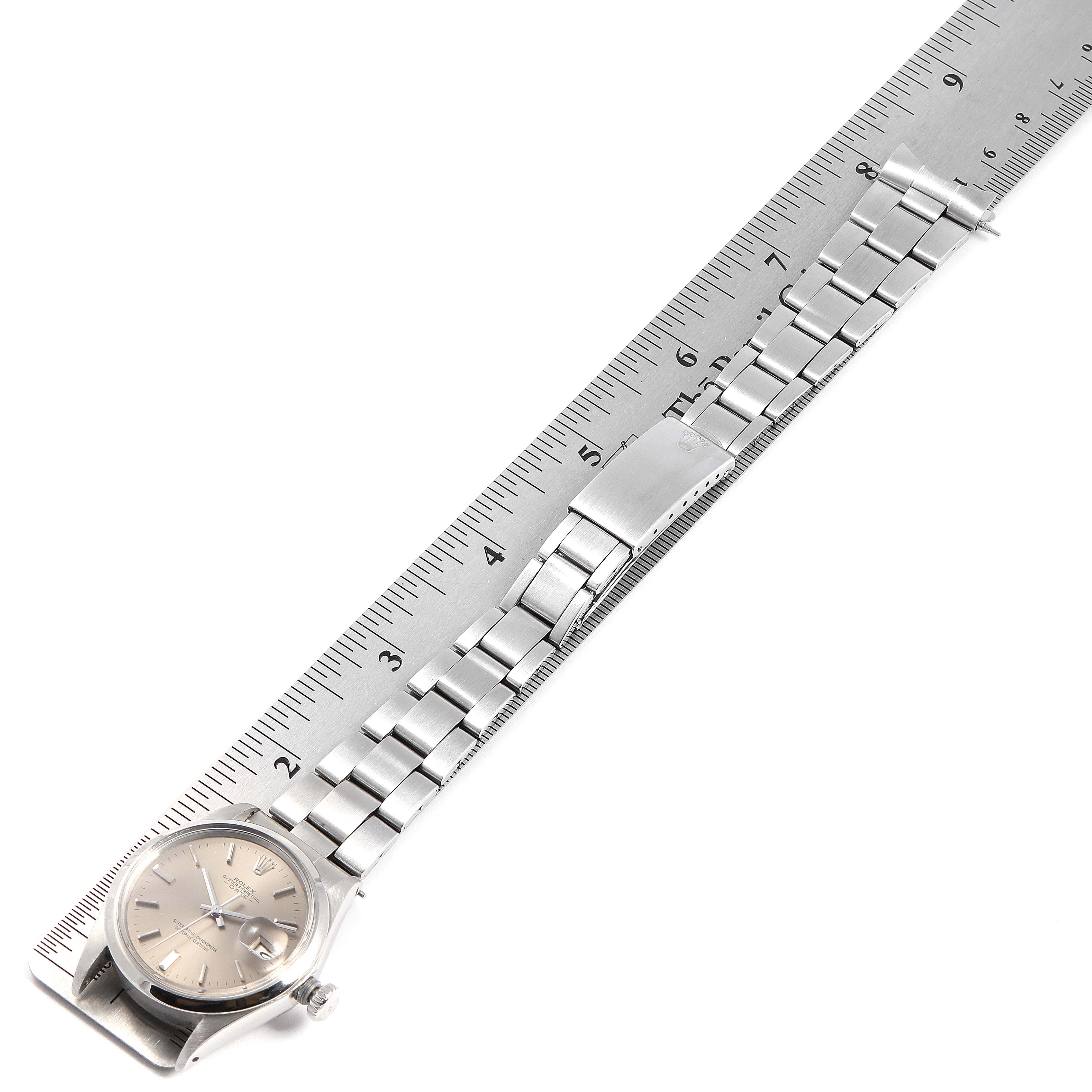 The image shows a Rolex Date 1500 Men's Stainless Steel Grey Dial 1500 Men's Stainless Steel Grey Dial model watch laid flat on a ruler, displaying the full bracelet and face.