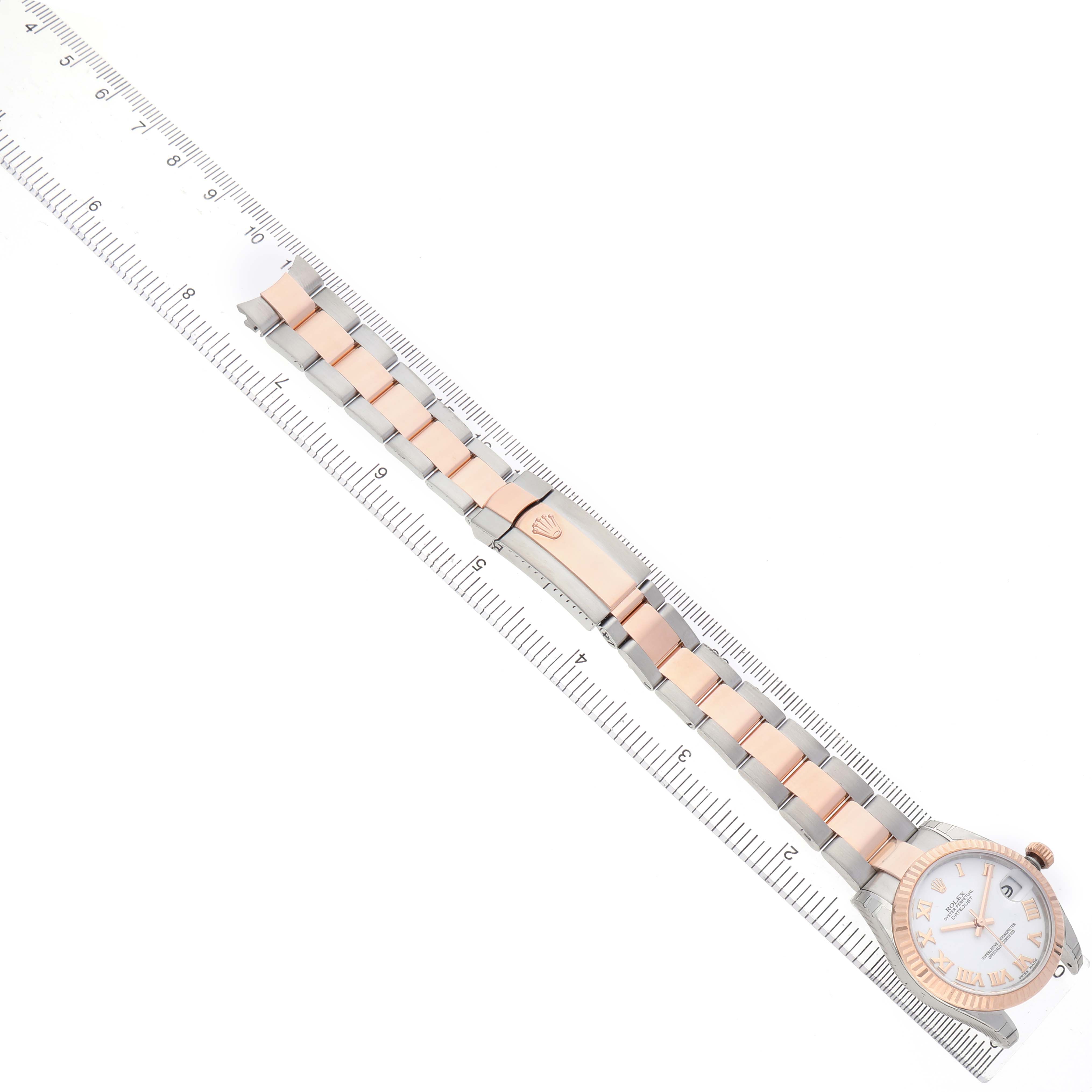 The Rolex Datejust 178271 Women's Stainless Steel White Dial watch is shown from a top-down angle, displaying the entire band and dial alongside a ruler for scale.